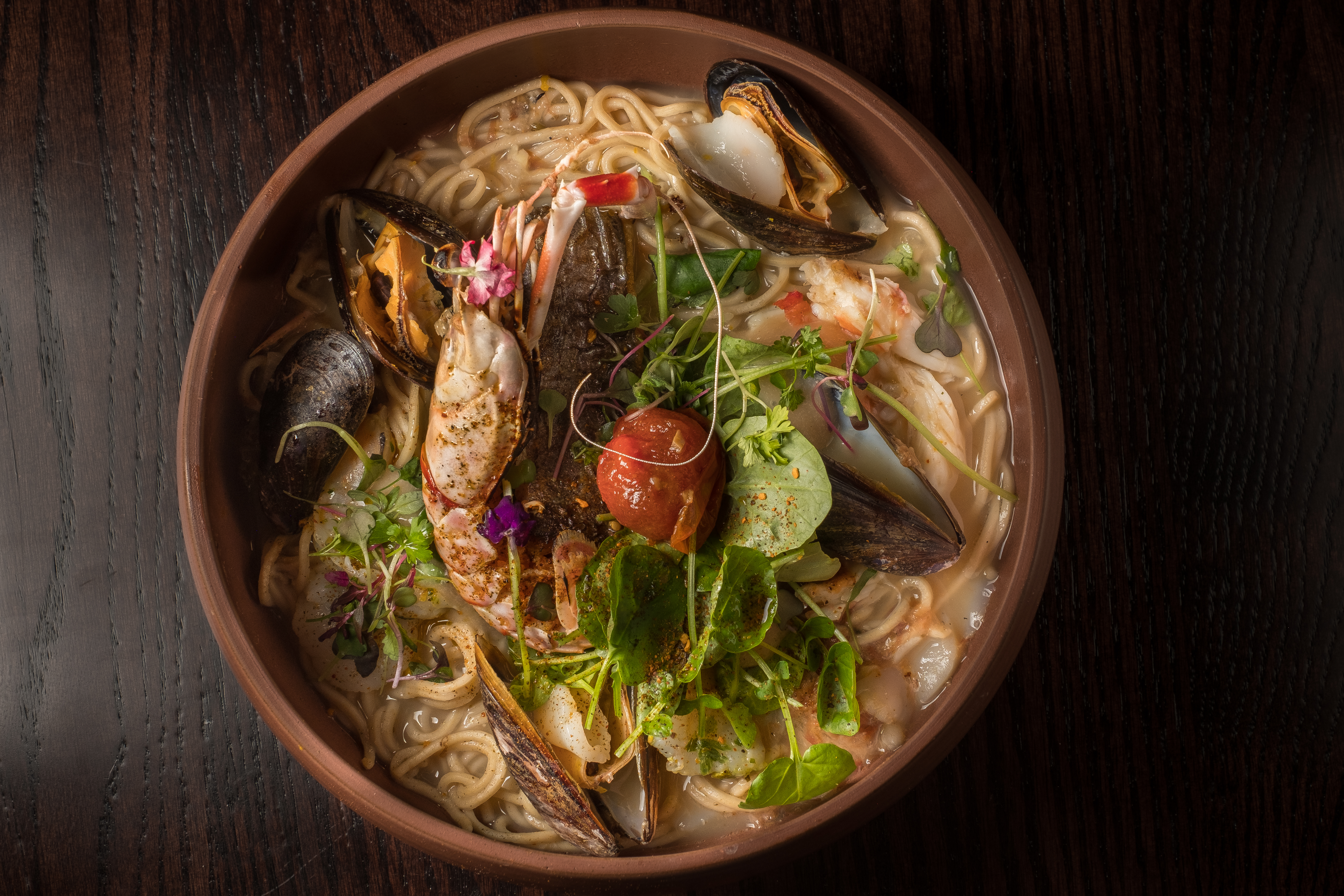 A closeup of an earthenware bowl filled with ramen, broth, and topped with half a prawn
