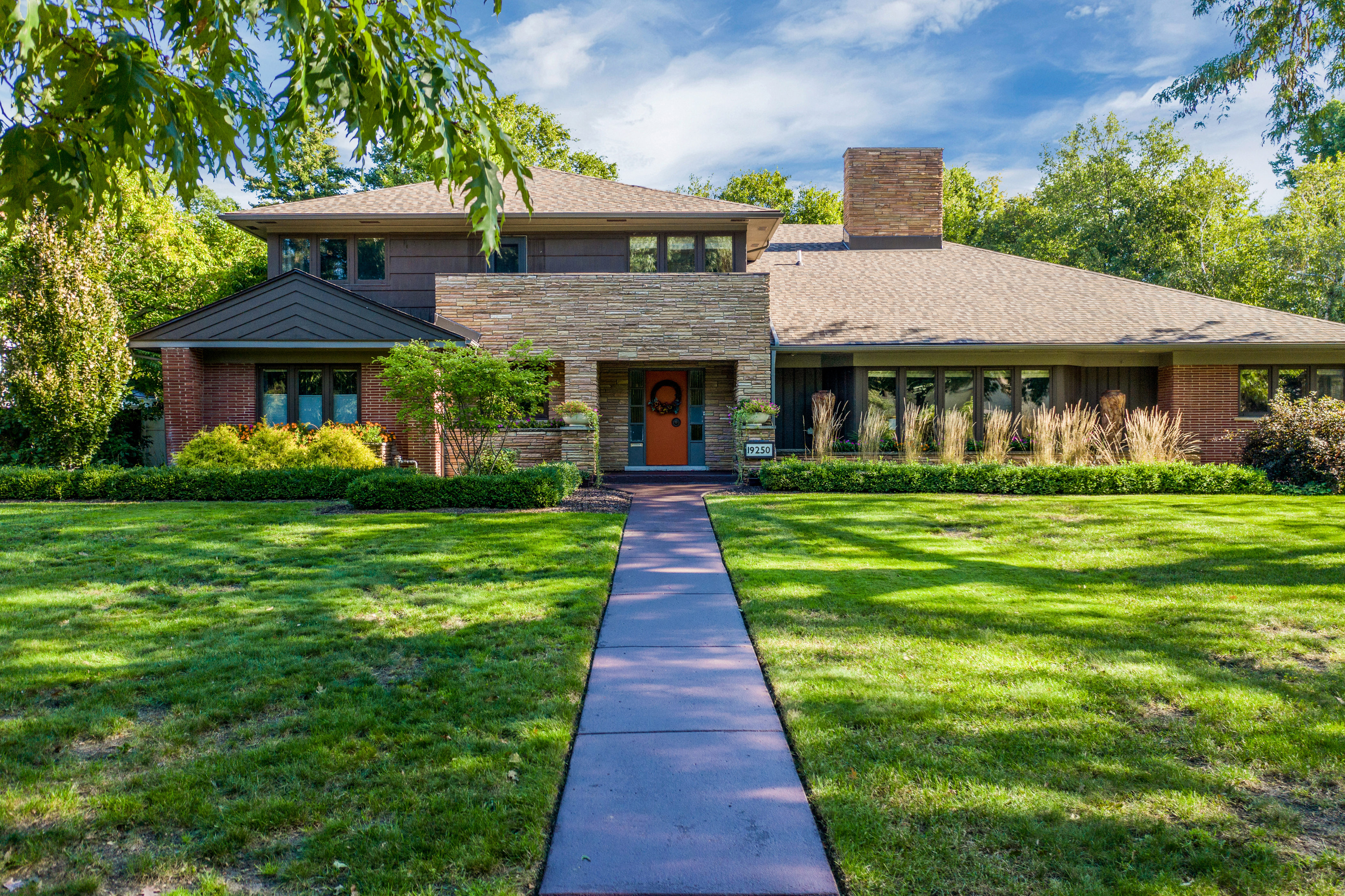 A large lawn and straight cement walkway leads to a long two-story home.