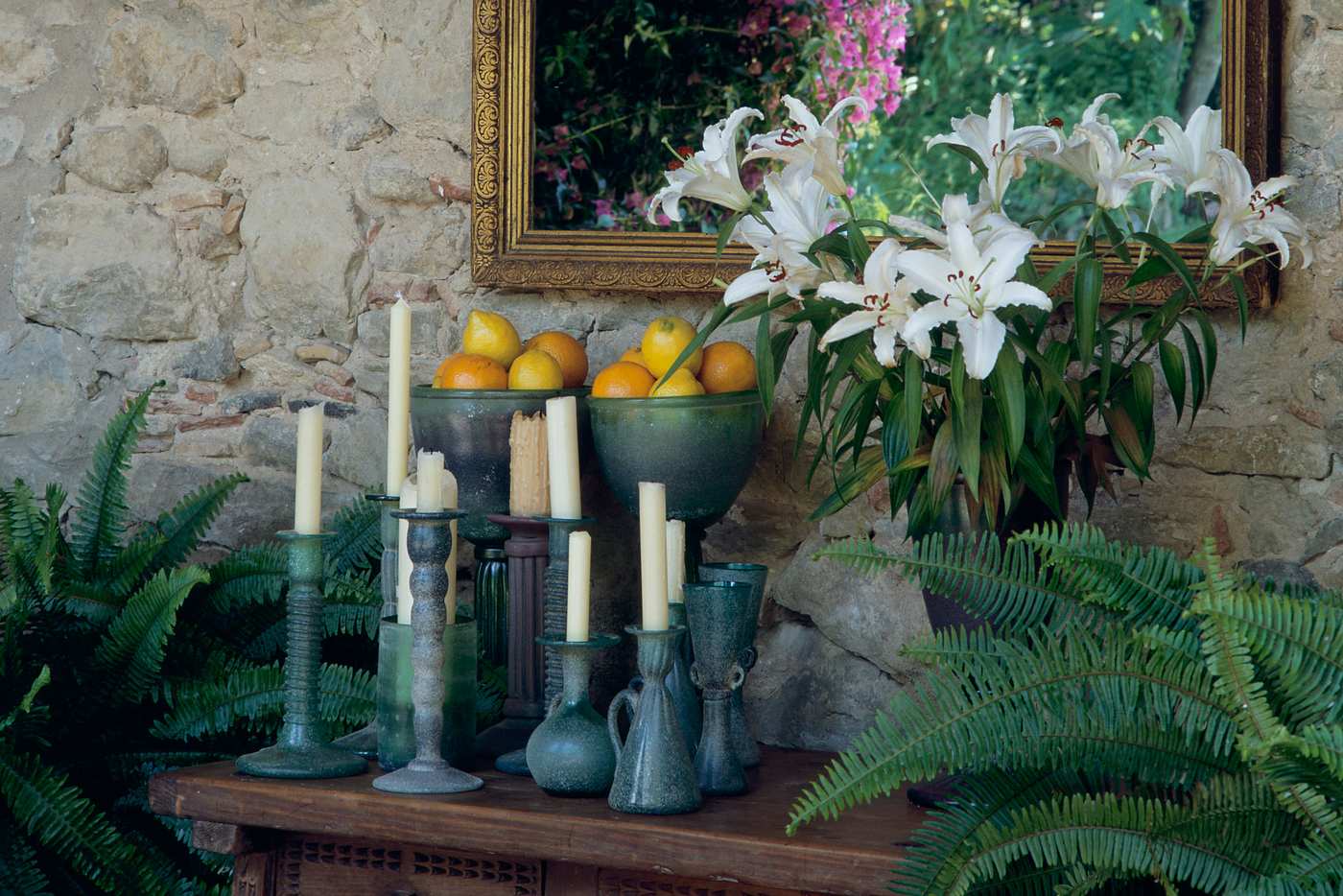 Blue candlestick holders with white candles on a wooden table, next to a vase of lilies. 