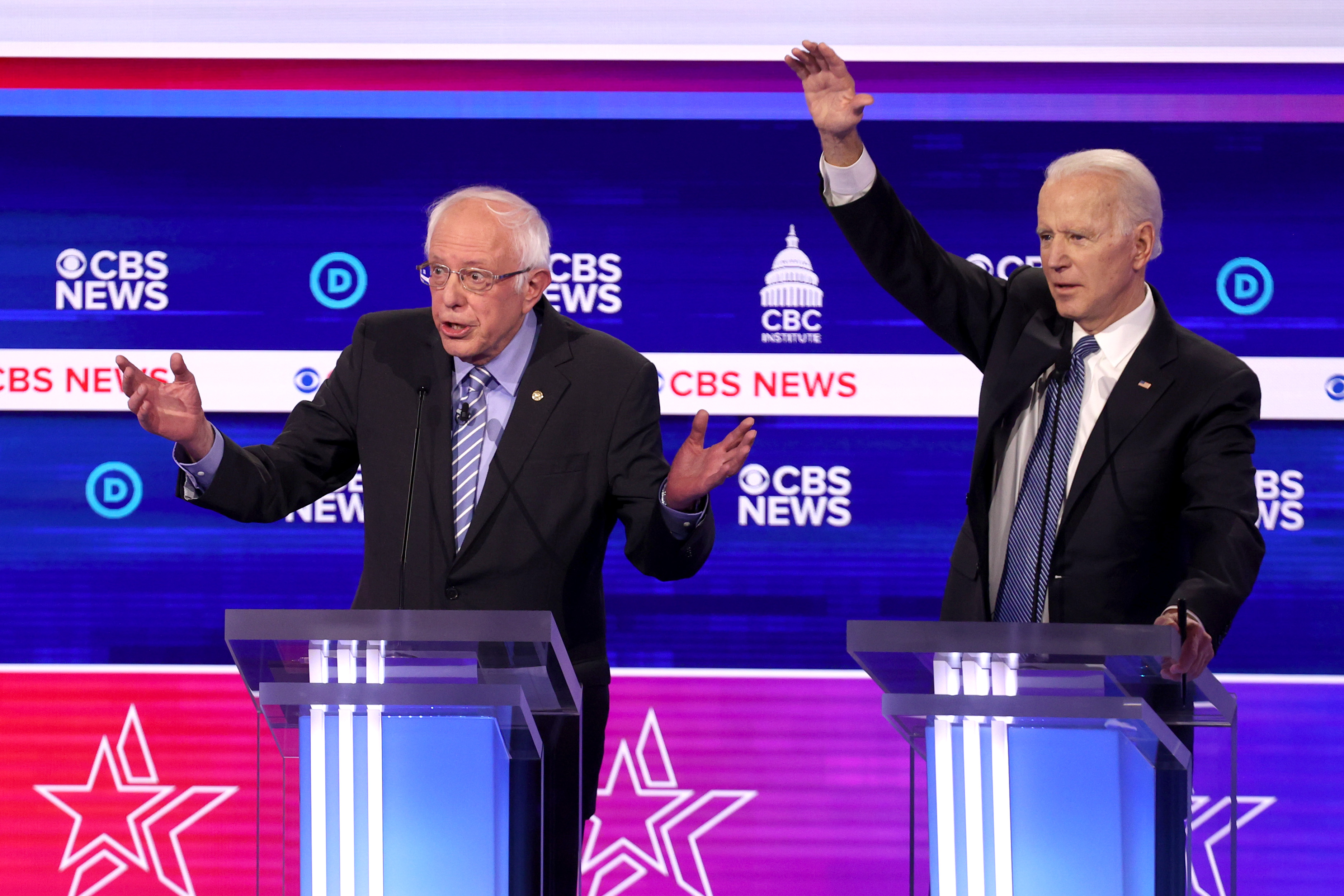 Senator Bernie Sanders and former Vice President Joe Biden stand onstage behind podiums with their arms raised.