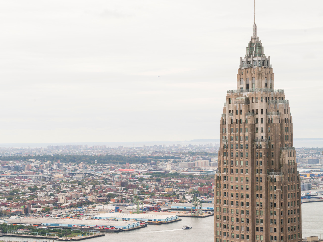 A landscape photo of the top spire of a building against the backdrop of New York City
