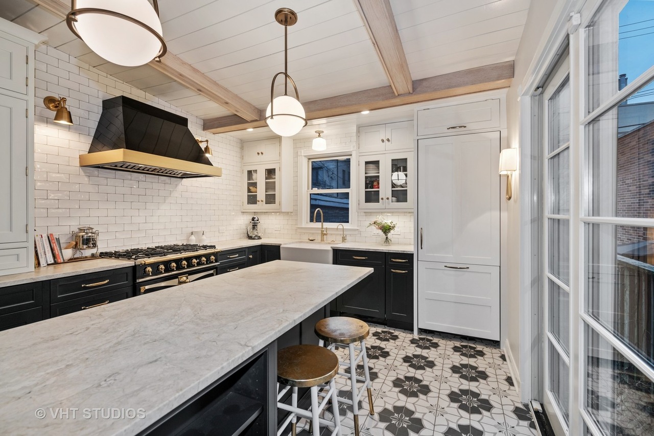 A kitchen with a large island, navy cabinets, white tile backsplash, and gold light fixtures.