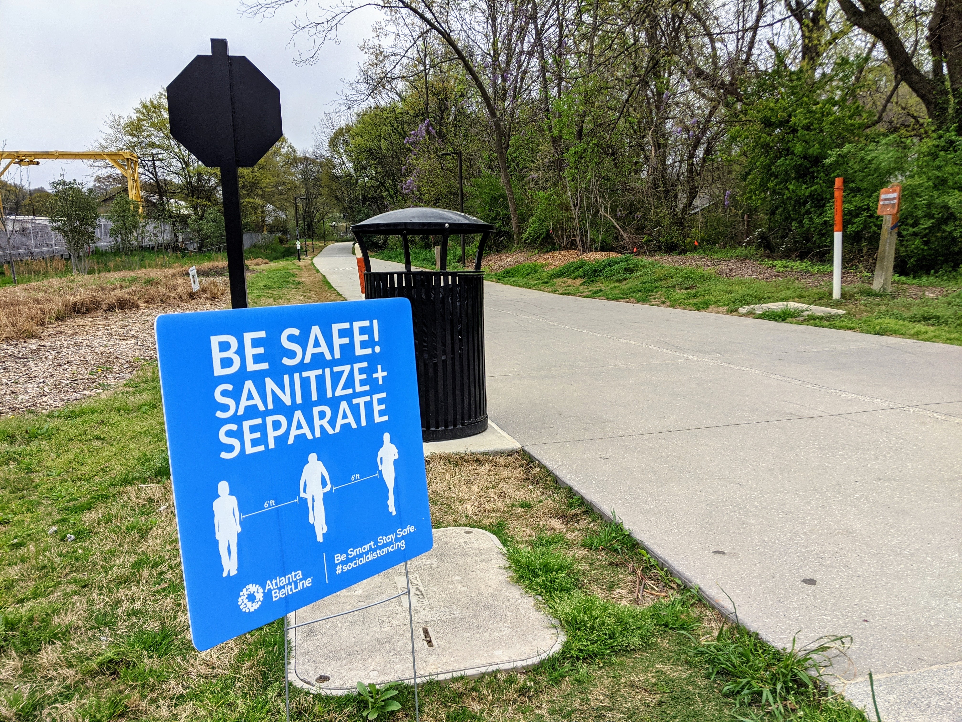 A photo of the Atlanta Beltline with a sign beside it urging people to keep apart from each other.
