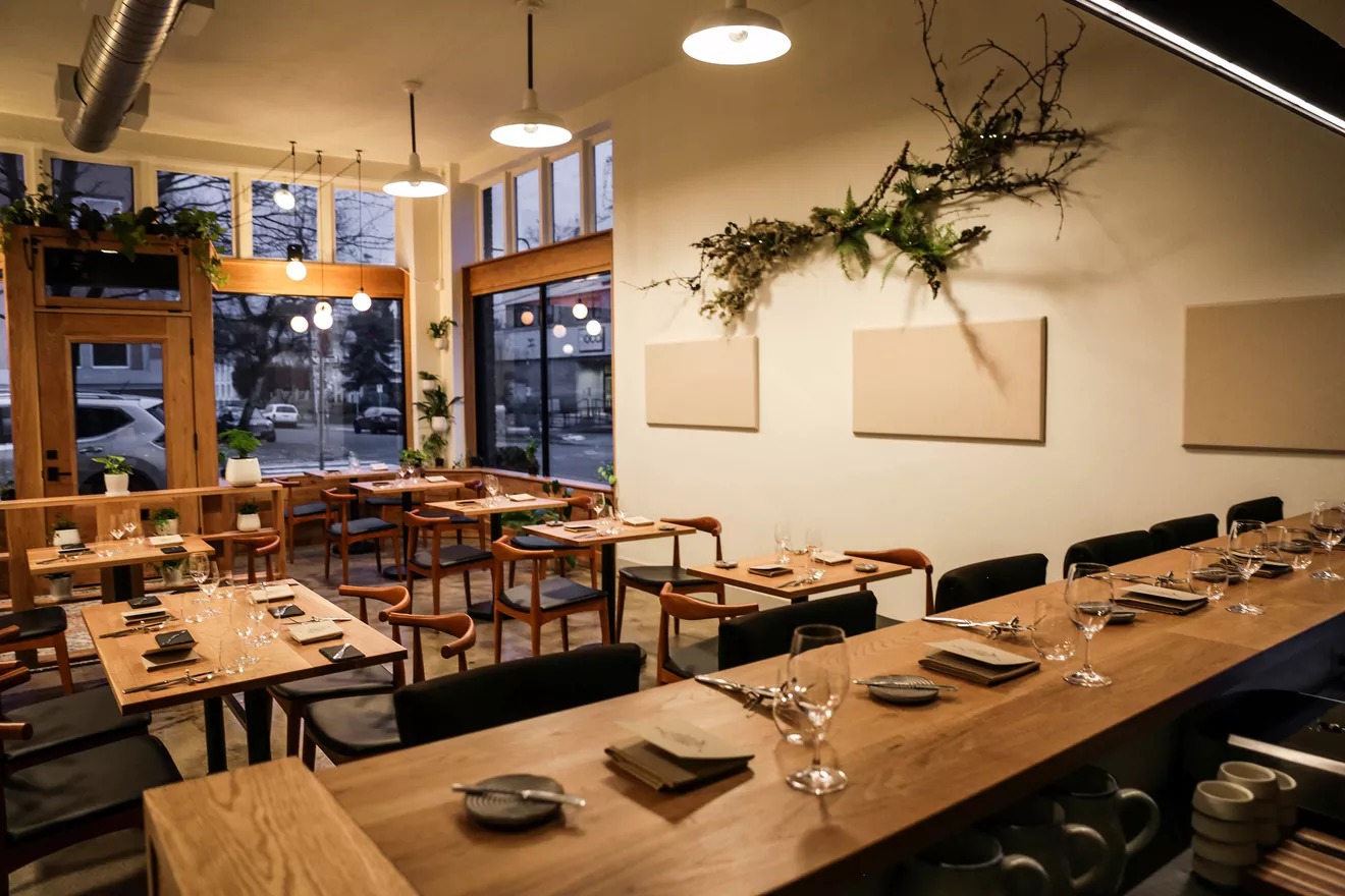 The dining room of Farm Spirit has several small wooden tables with wishbone chairs, a wooden chef’s counter looking into the kitchen, and living plant installations