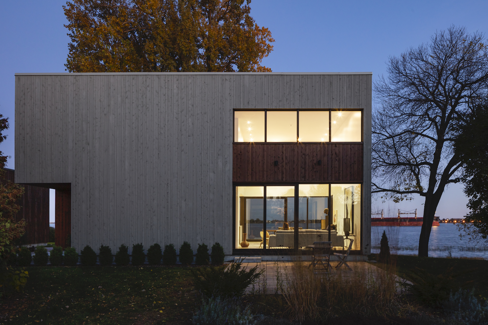 A rectangular house with large glass wall that offers view out to lake in the back.