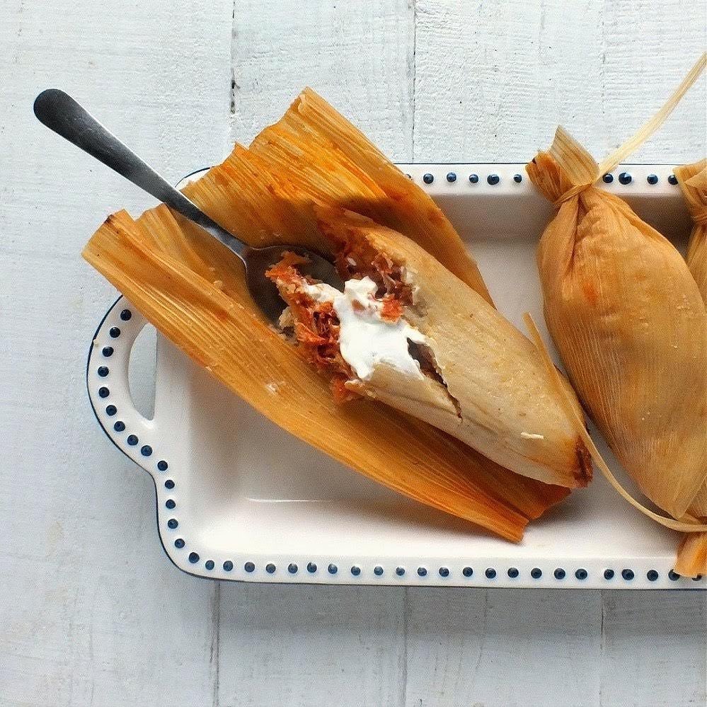 A tamale wrapped in a corn husk with a spoon inside.