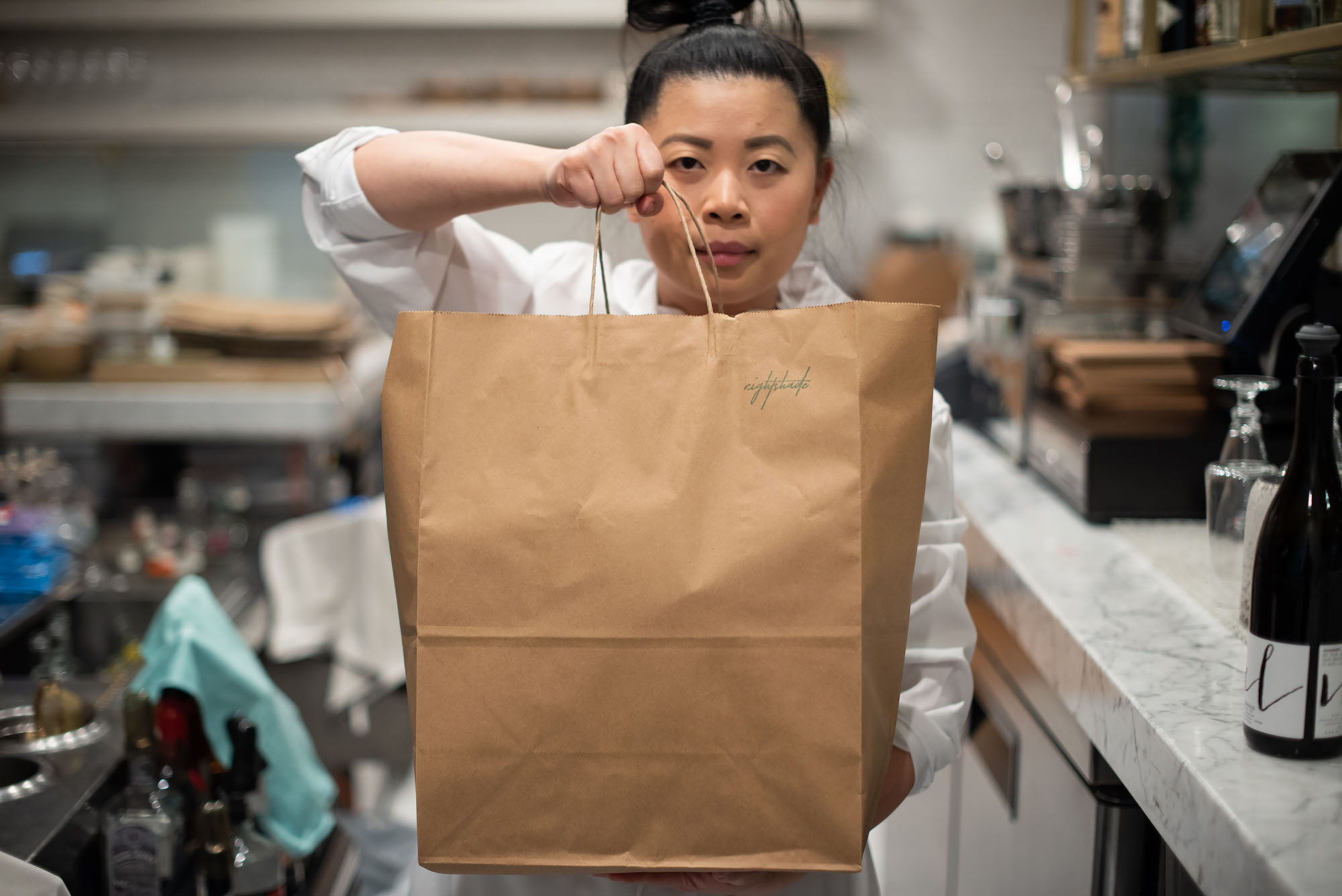 Nightshade owner and chef Mei Lin holds a brown bag of takeout inside her LA restaurant.
