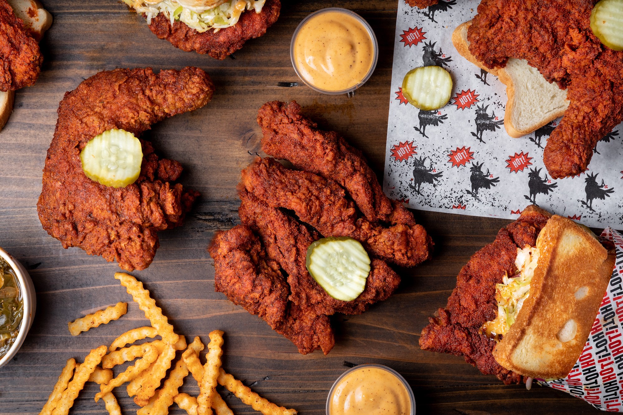 A spread out collection of hot chicken, fries, and sauces from Howlin’ Ray’s.