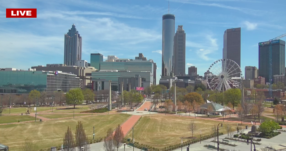A screenshot of a park in Atlanta with a lawn and grass and tall buildings. 