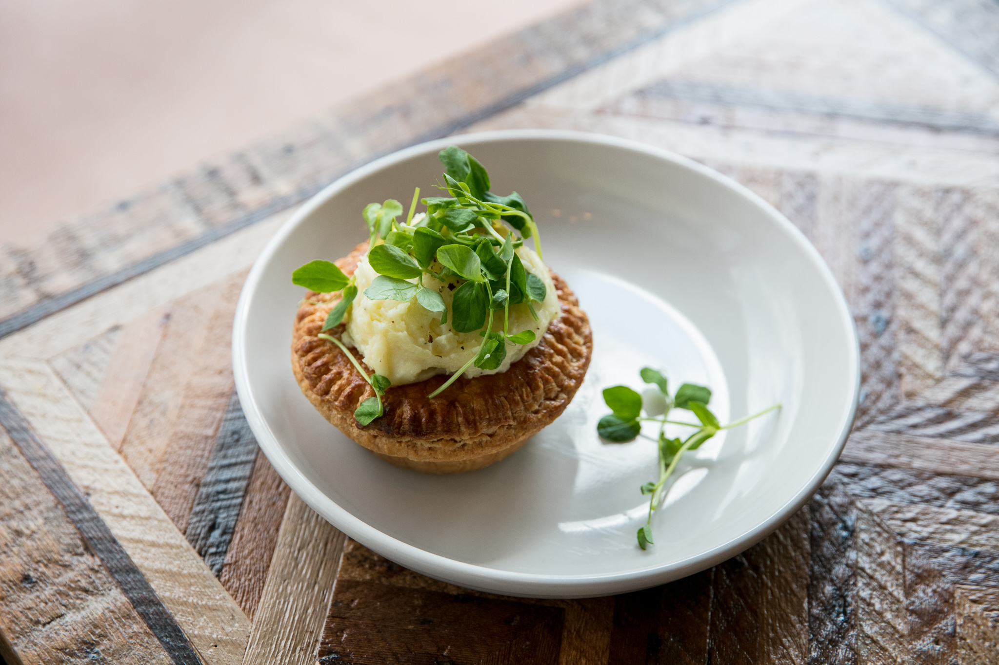The Aussie meat pie from folk is shown on a plate with mashed potatoes on top and pea shoots. 