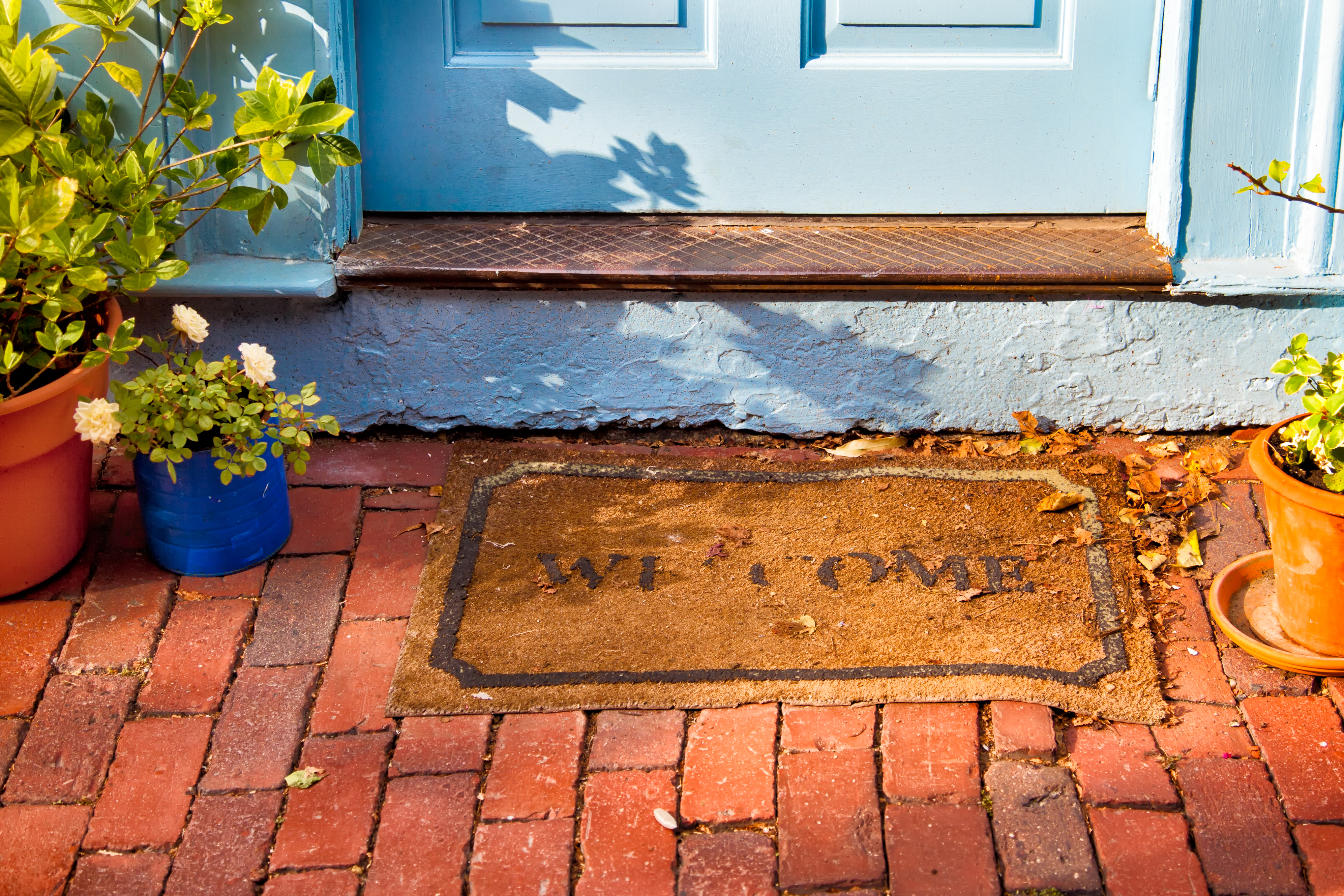 A welcome mat at the outside foot of a door on a brick path.