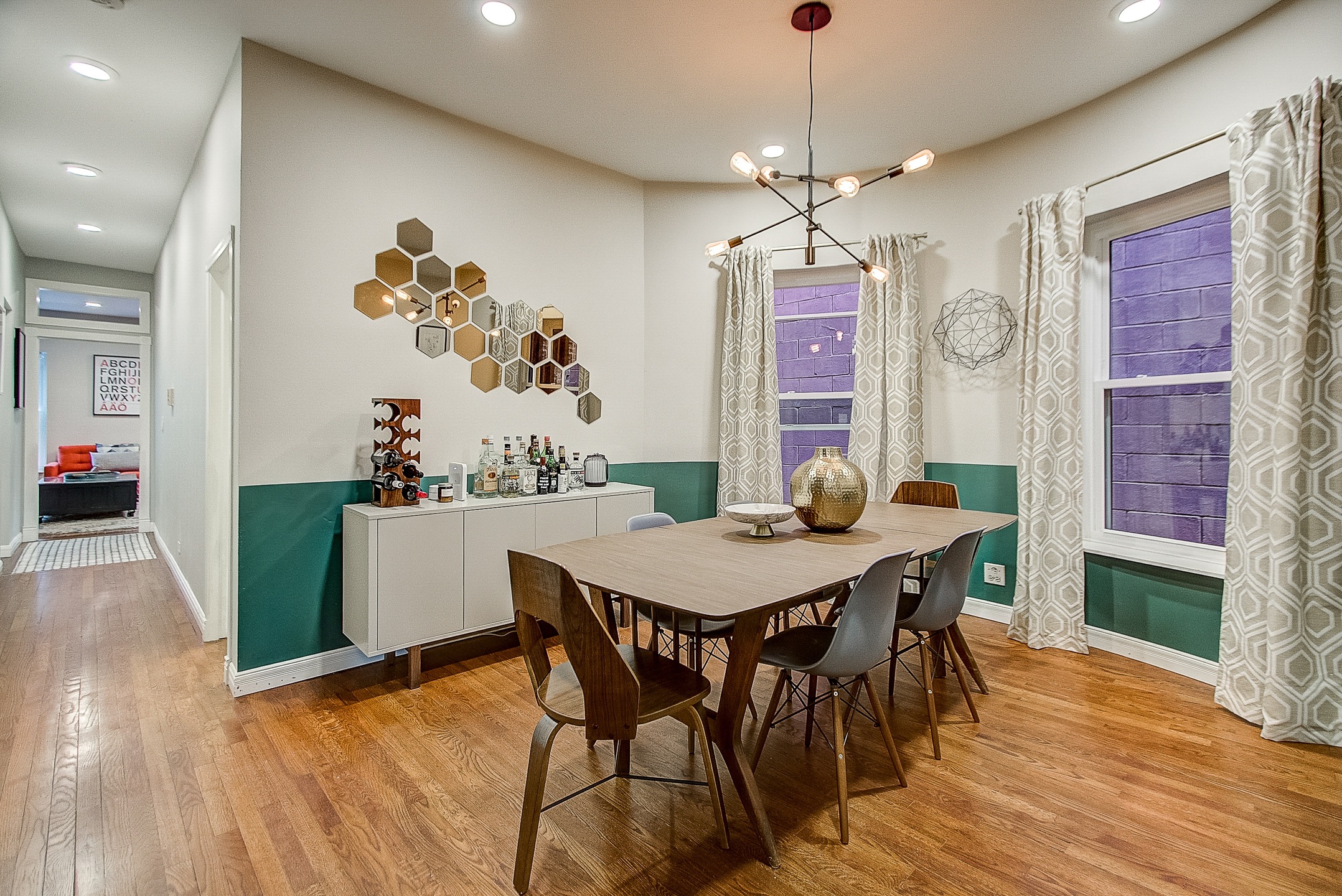 A dining room with a green accent wall and an industrial light fixture, bar, and dining table. 
