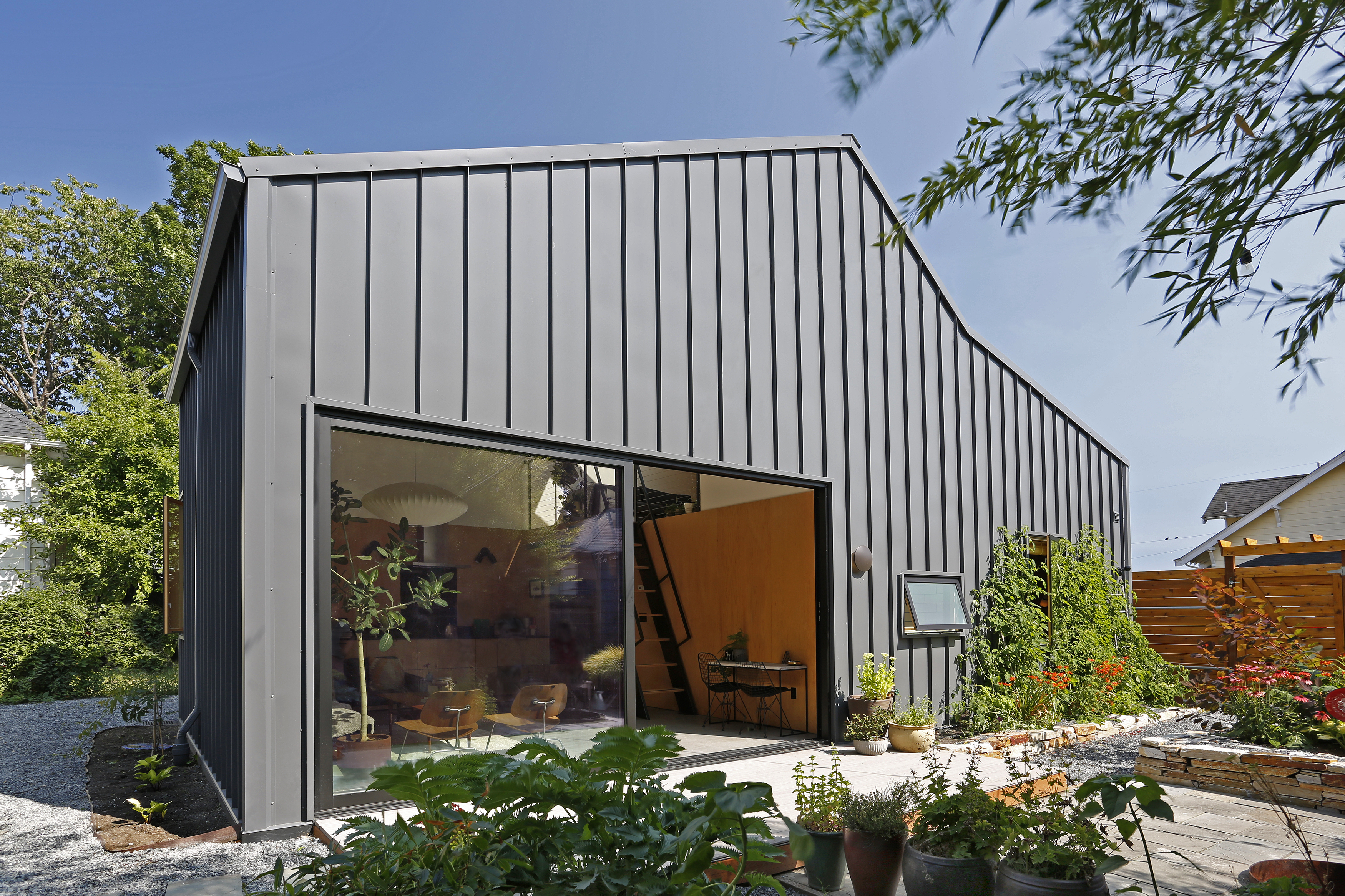 Single-story home with angled ceiling and black metal panels. A large sliding door opens to a garden.