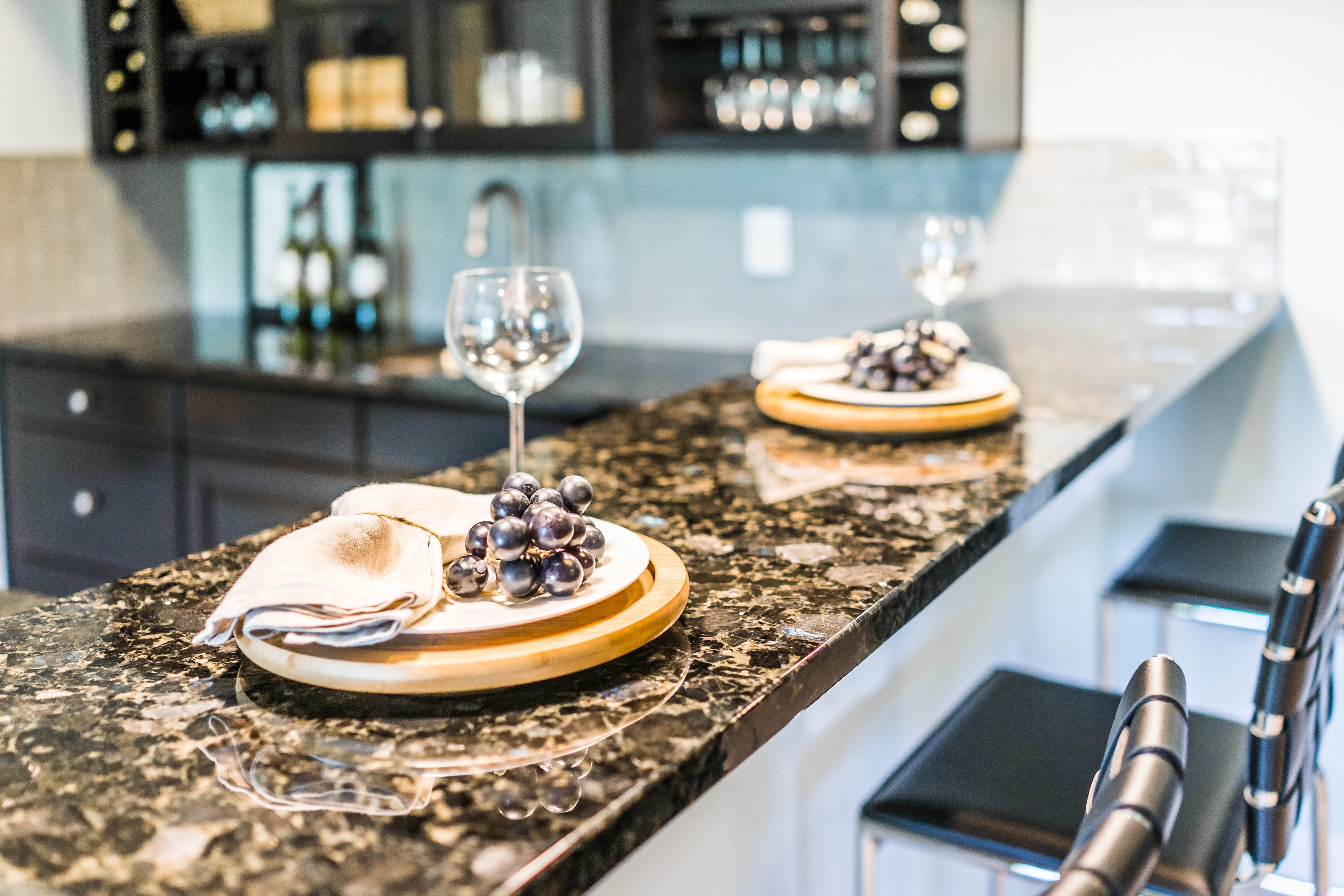 Two place arrangements on a kitchen counter, with wine glasses and fake grape bunches at each.