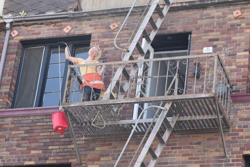 A home cook lowers food from her balcony using rope and a bright red bucket.