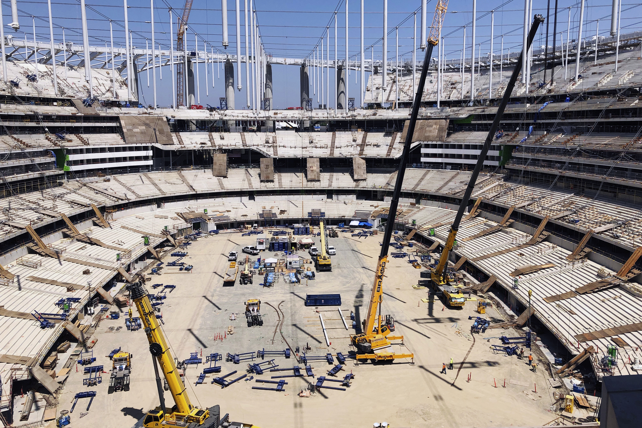 An aerial photo of an under-construction stadium, with a dirt floor and visible beams. 