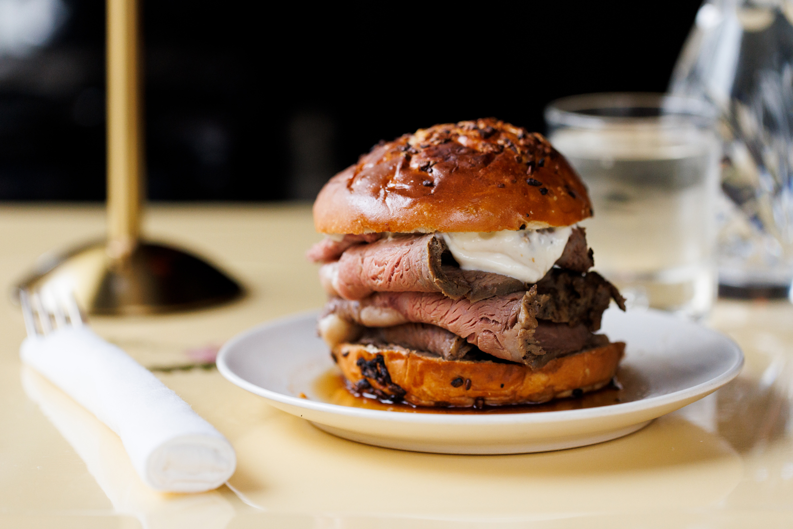 Three thick slice of tender roast beef topped with horseradish sauce sandwiched between a slice roasted onion brioche bun from Whoopsie’s cocktail lounge in Atlanta.
