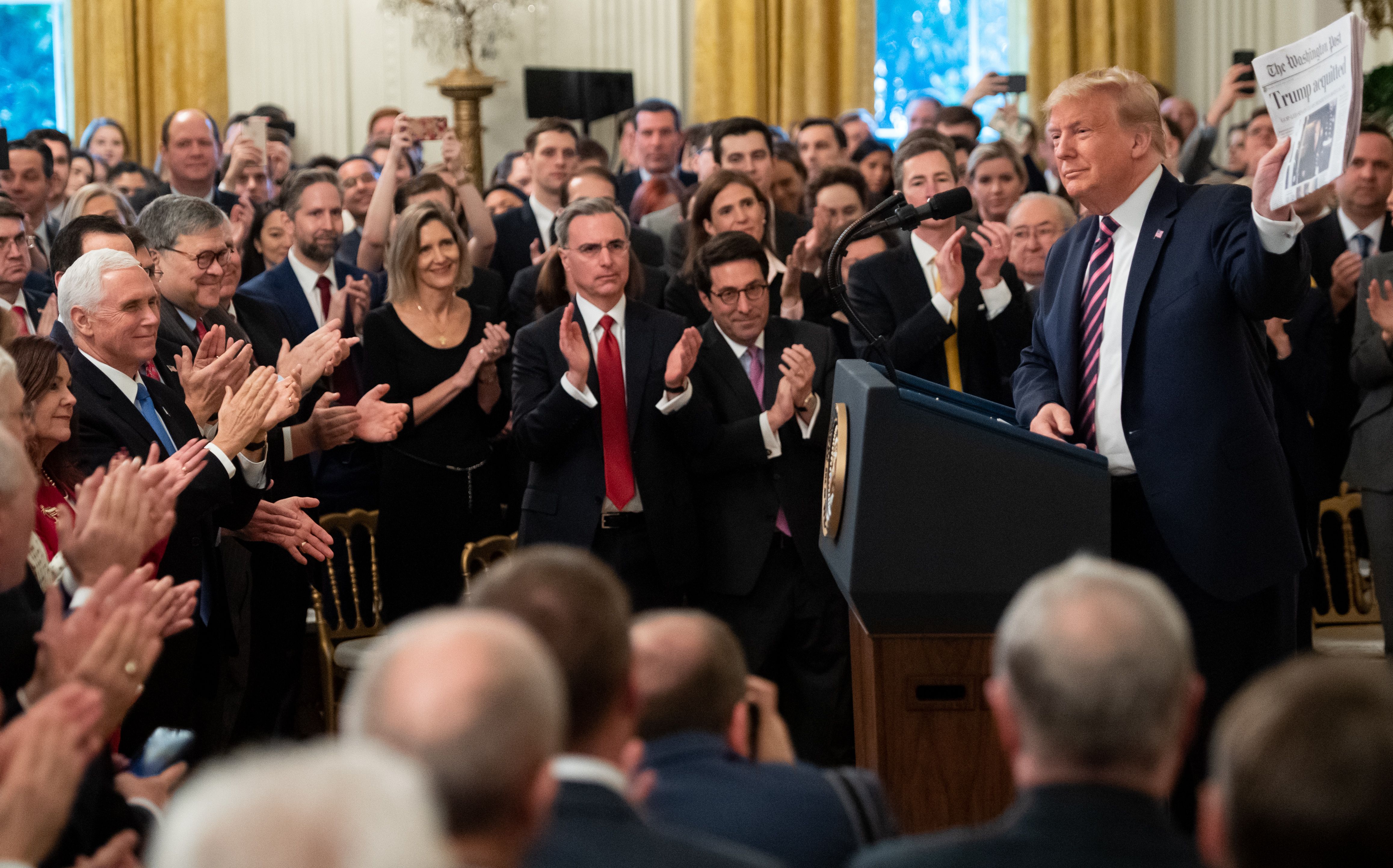 Trump holds up a Washington Post front page that says “Trump Acquitted” as notable Republicans including Vice President Mike Pence, AG Bill Barr, dozens of lawmakers, and members of his impeachment defense team applaud him. 