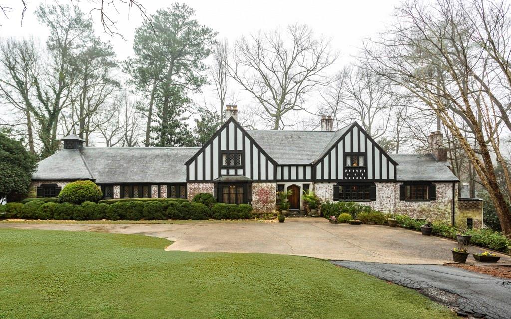A huge Tudor home with a lot of trees around it on a large lot.