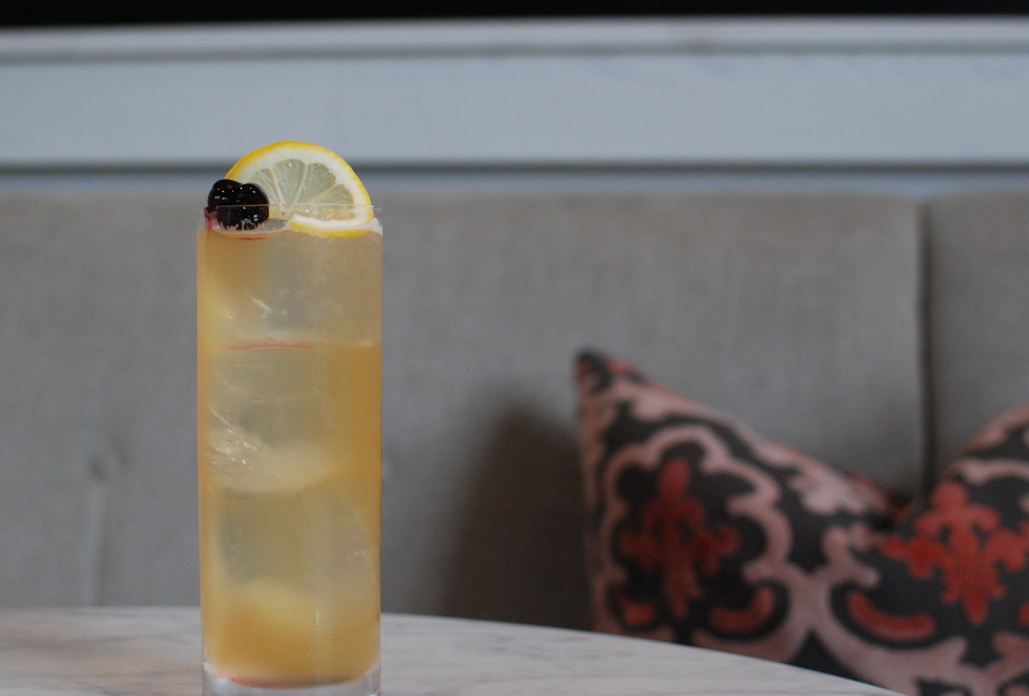 A tall glass with a yellow effervescent beverage garnished with a lemon wheel.