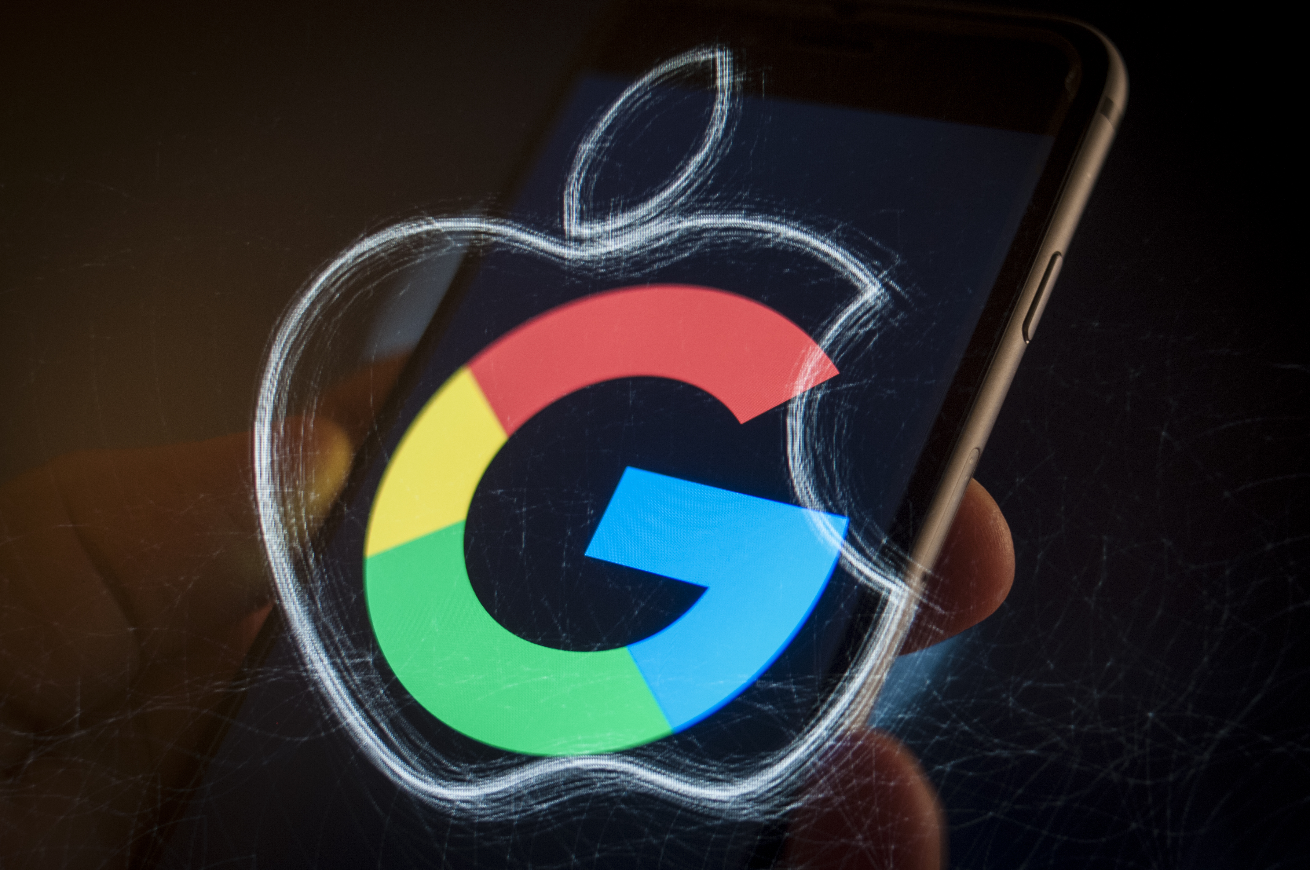 The Google G logo and the Apple logo superimposed on a smartphone held in a hand.