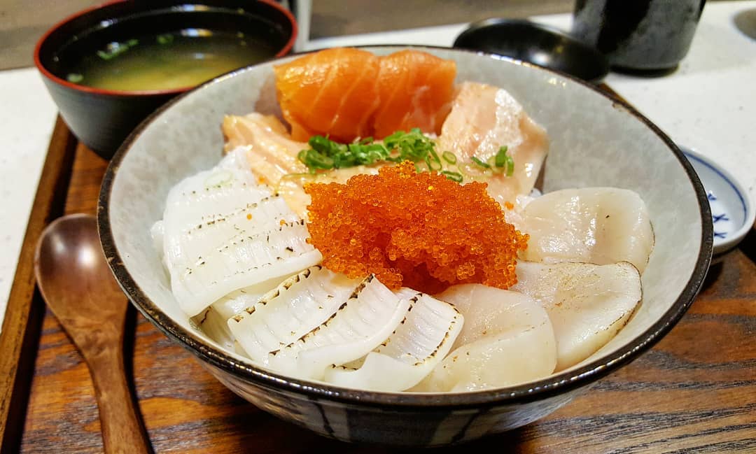 A bowl of raw seafood, including salmon and salmon roe, on rice, served on a wooden tray with miso soup