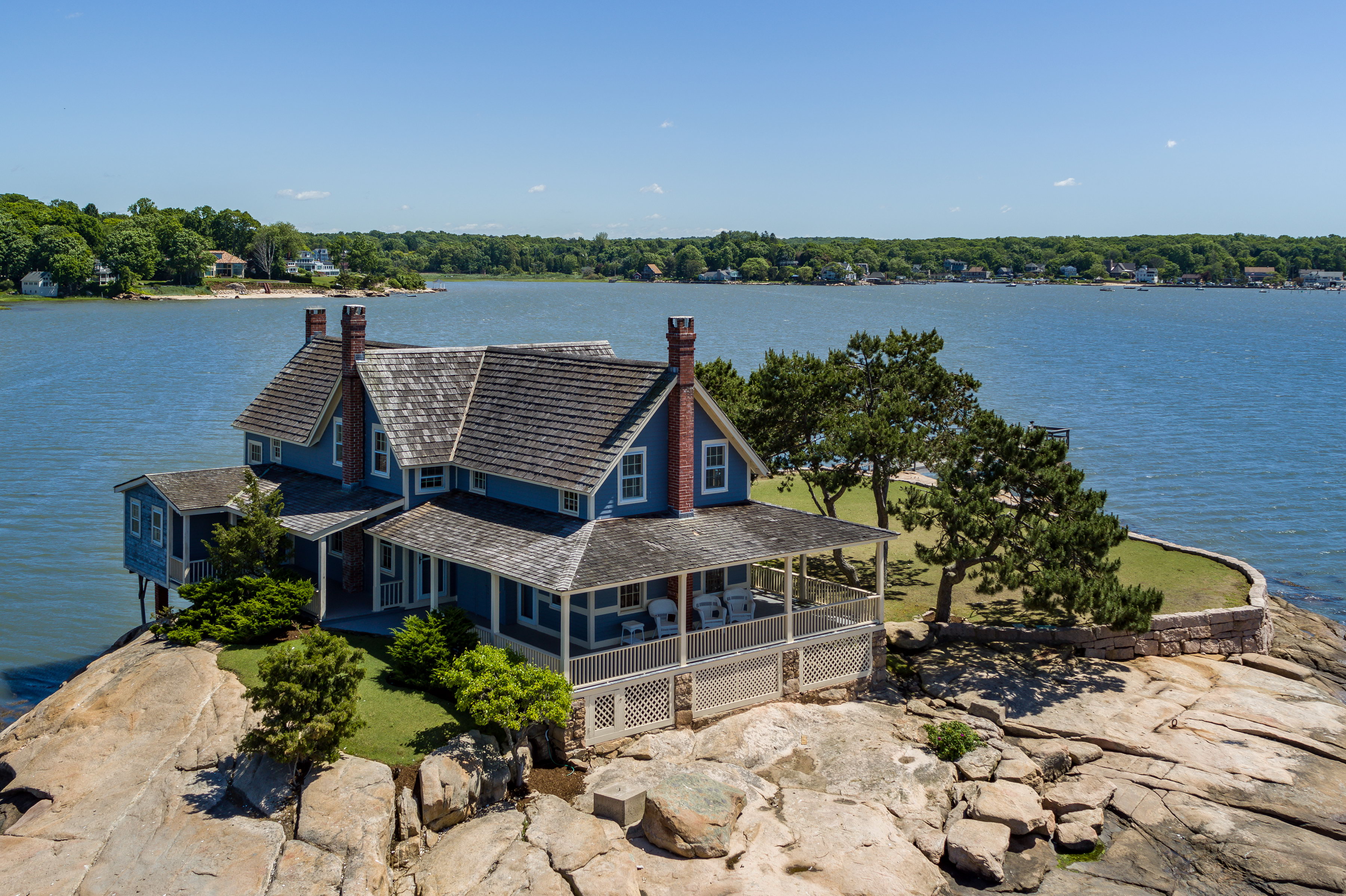 An exterior view of a cottage on a rocky island with water all around it. 