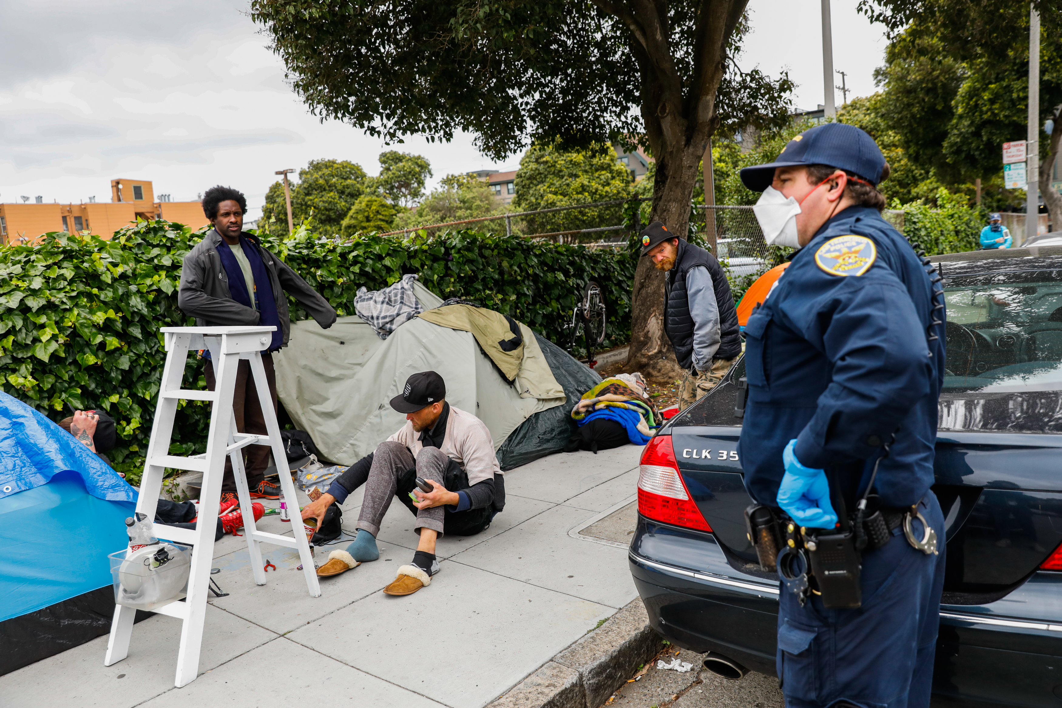 A police officer asks a group of homeless men to social distance themselves.