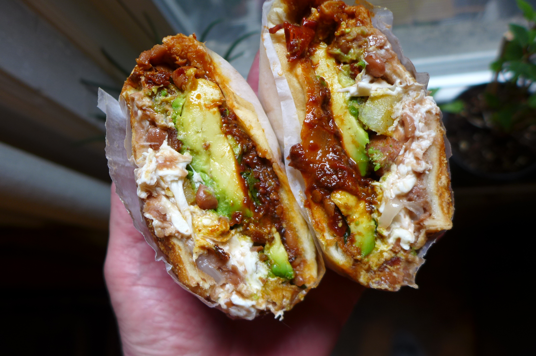 A hand holds the two halves of a cemita.