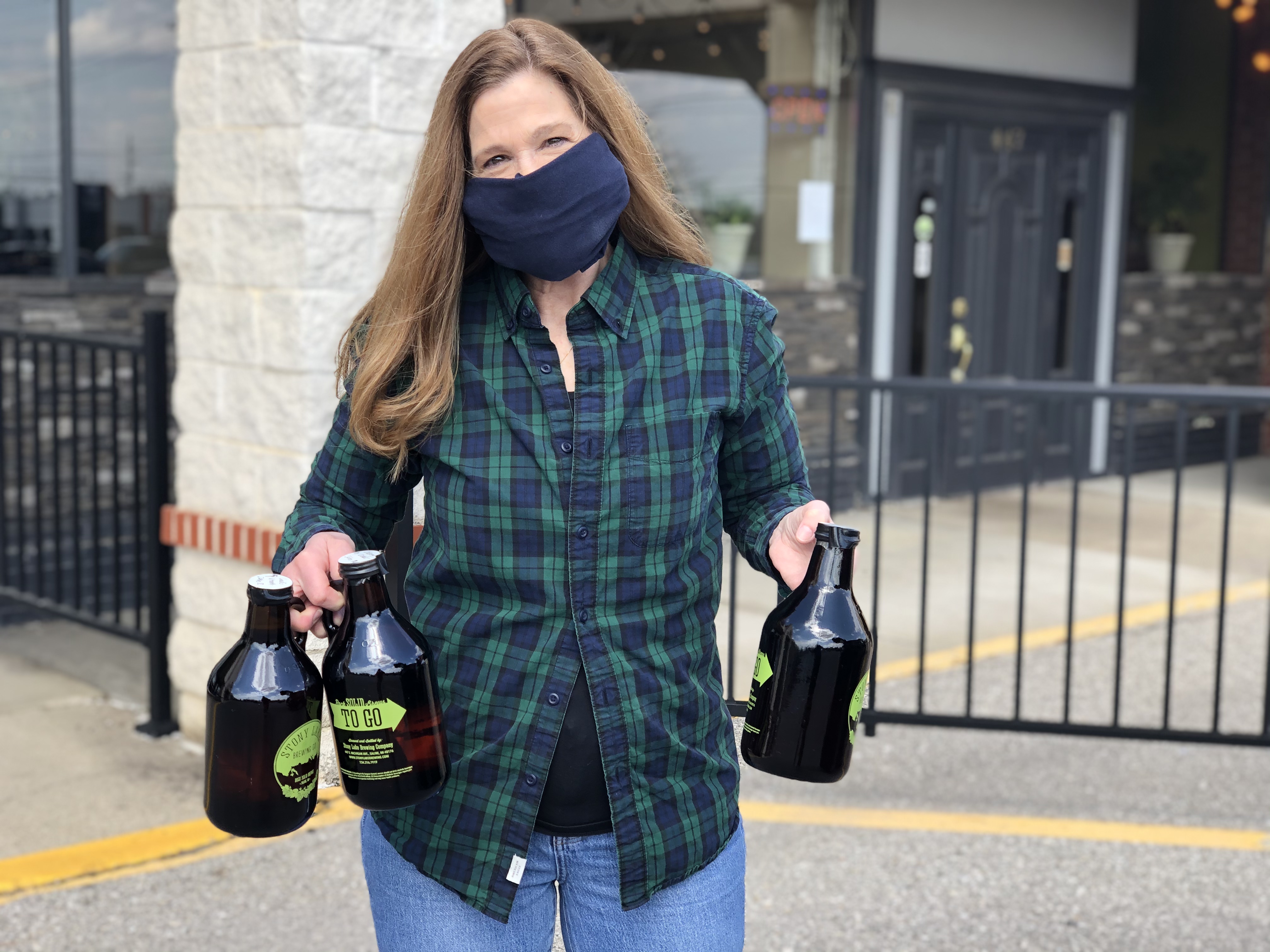 A woman with long hair and a facemask delivers curbside growlers. 