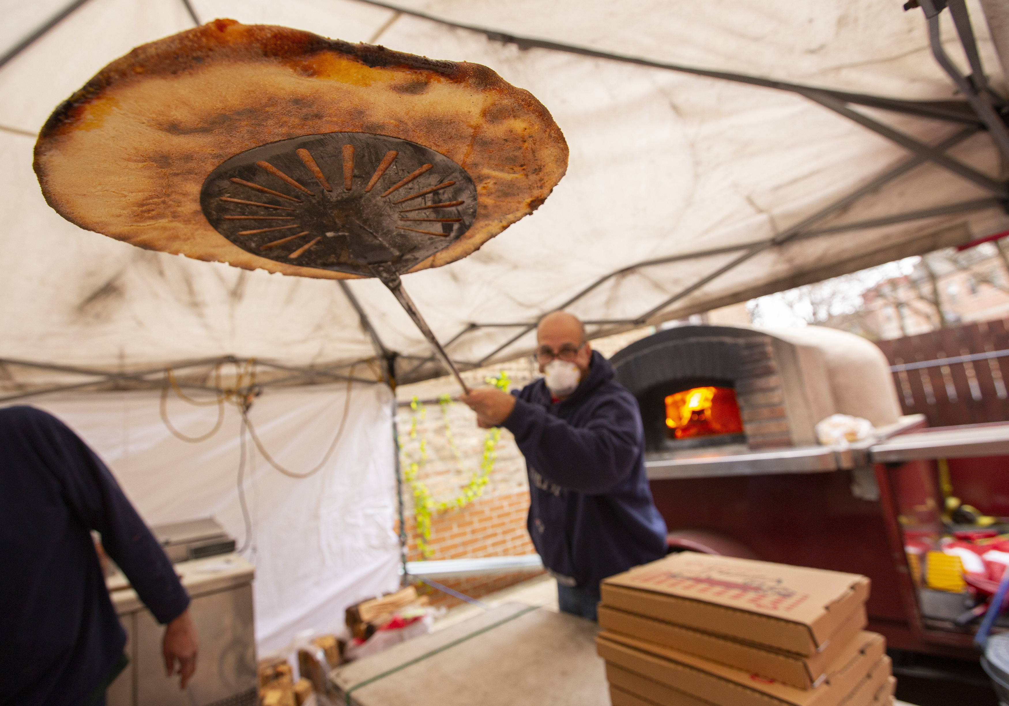 A man lifts a pizza out of an wood-burning oven outside.