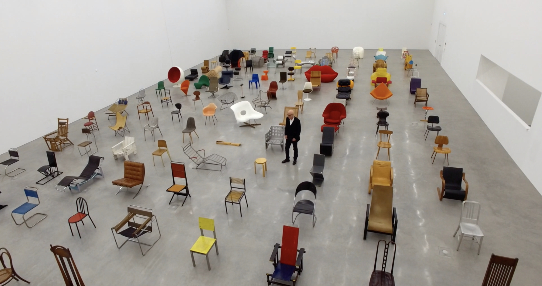 A man stands among a sea of different kinds of chairs.