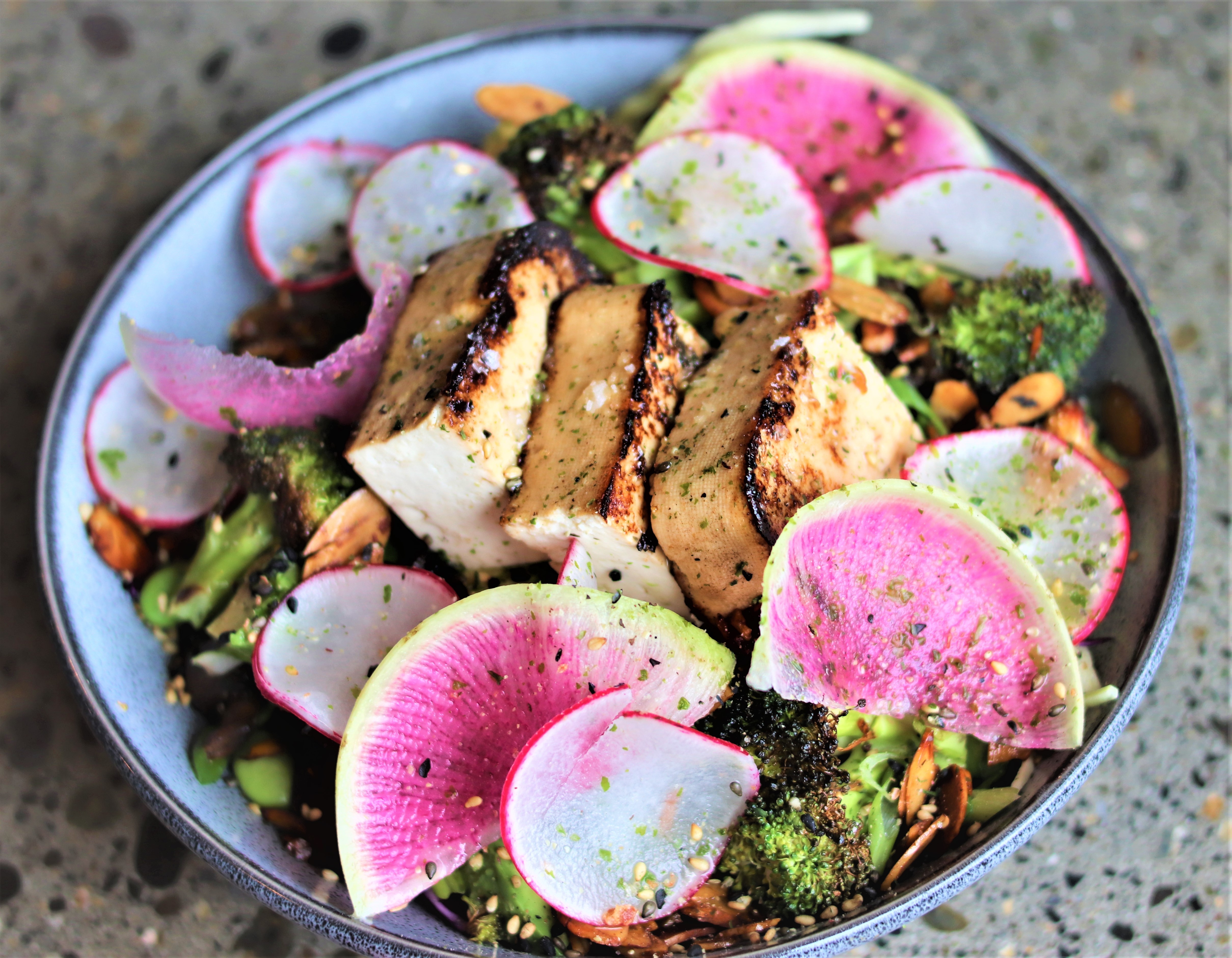 Three pieces of tofu sit on a bowl of greens with slices of watermelon radish
