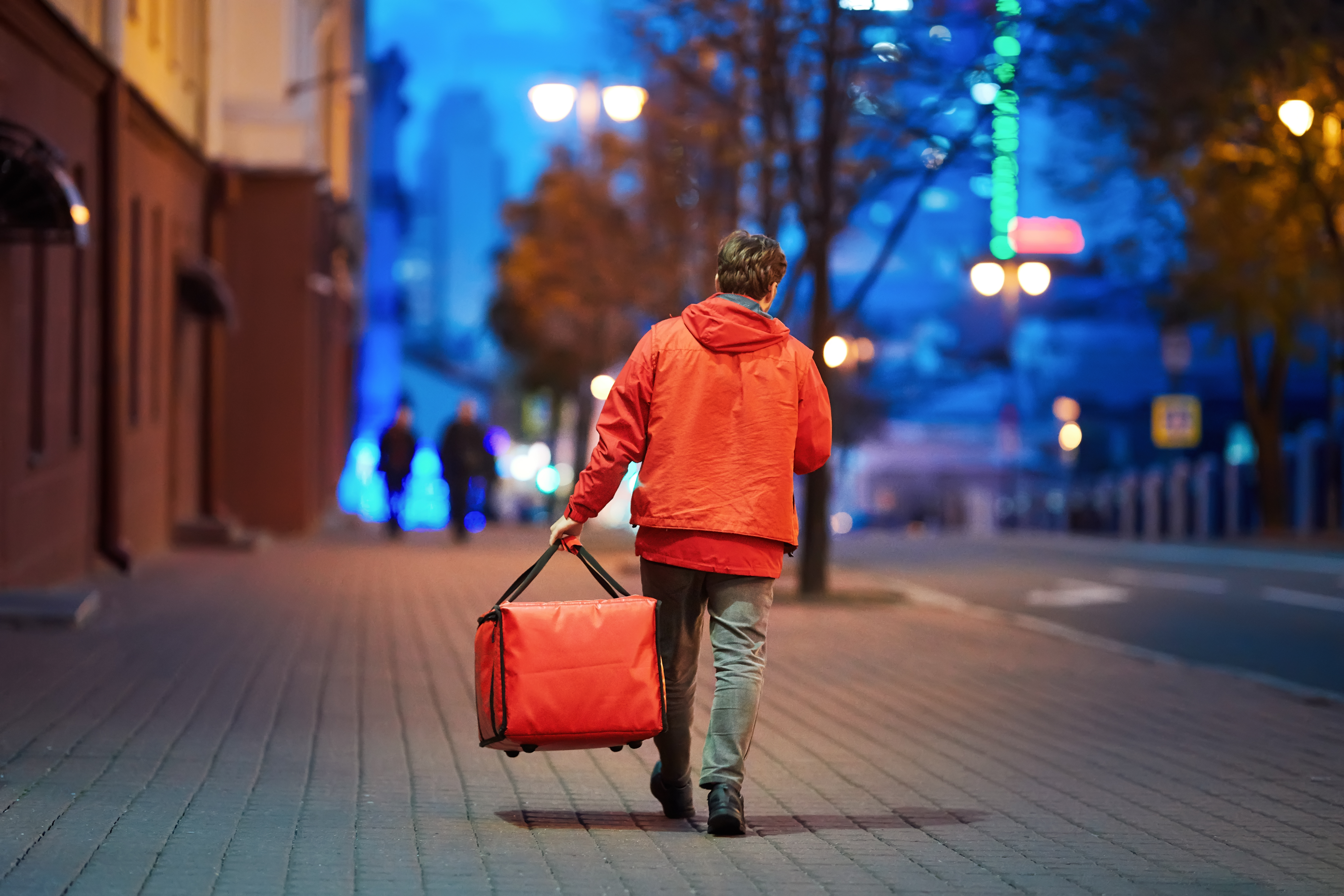 一名快递员拿着一个红色的保暖包走在空旷的街道上。