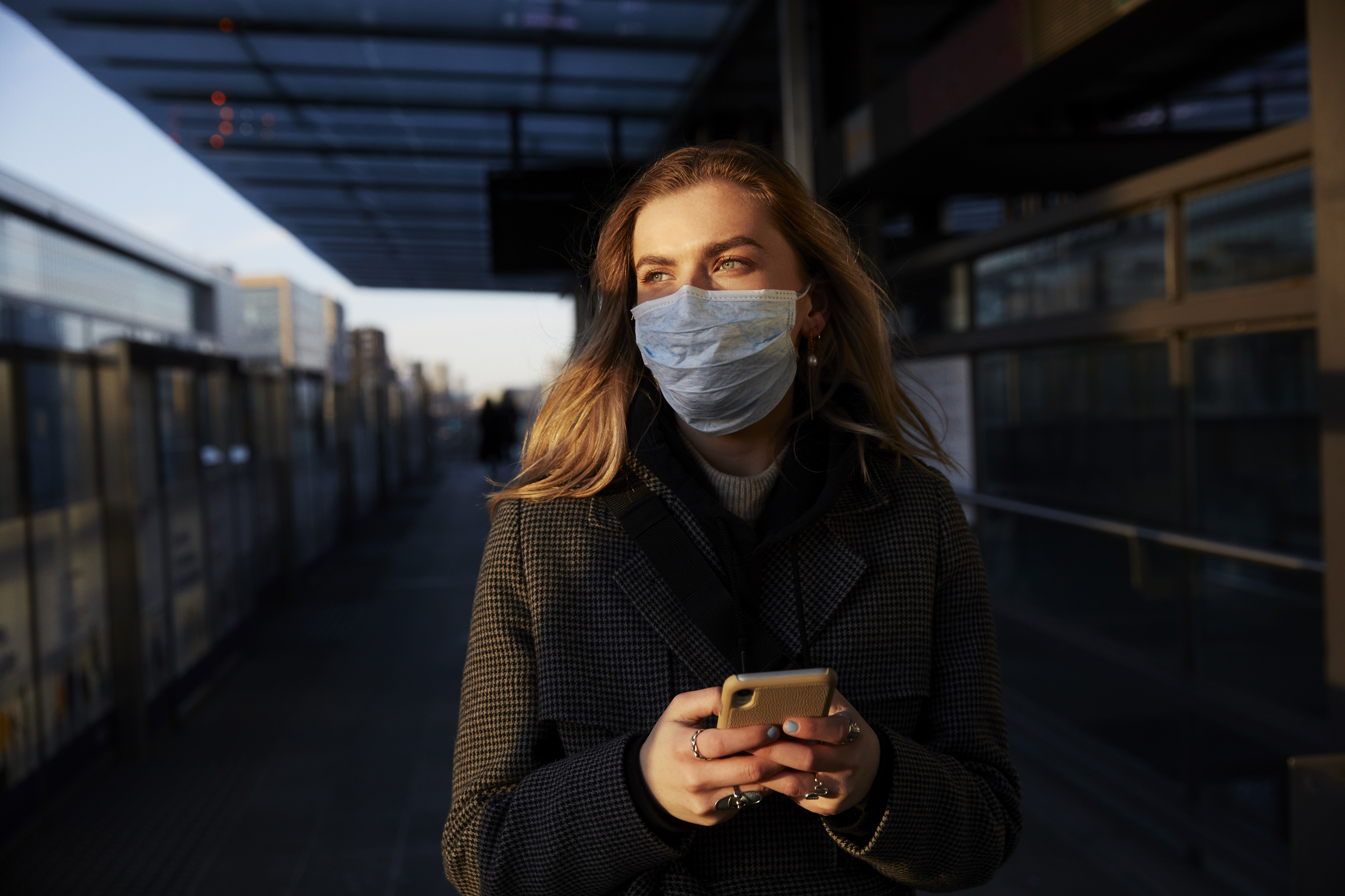 A person wearing a breathing mask holds a cellphone while standing on a city street.
