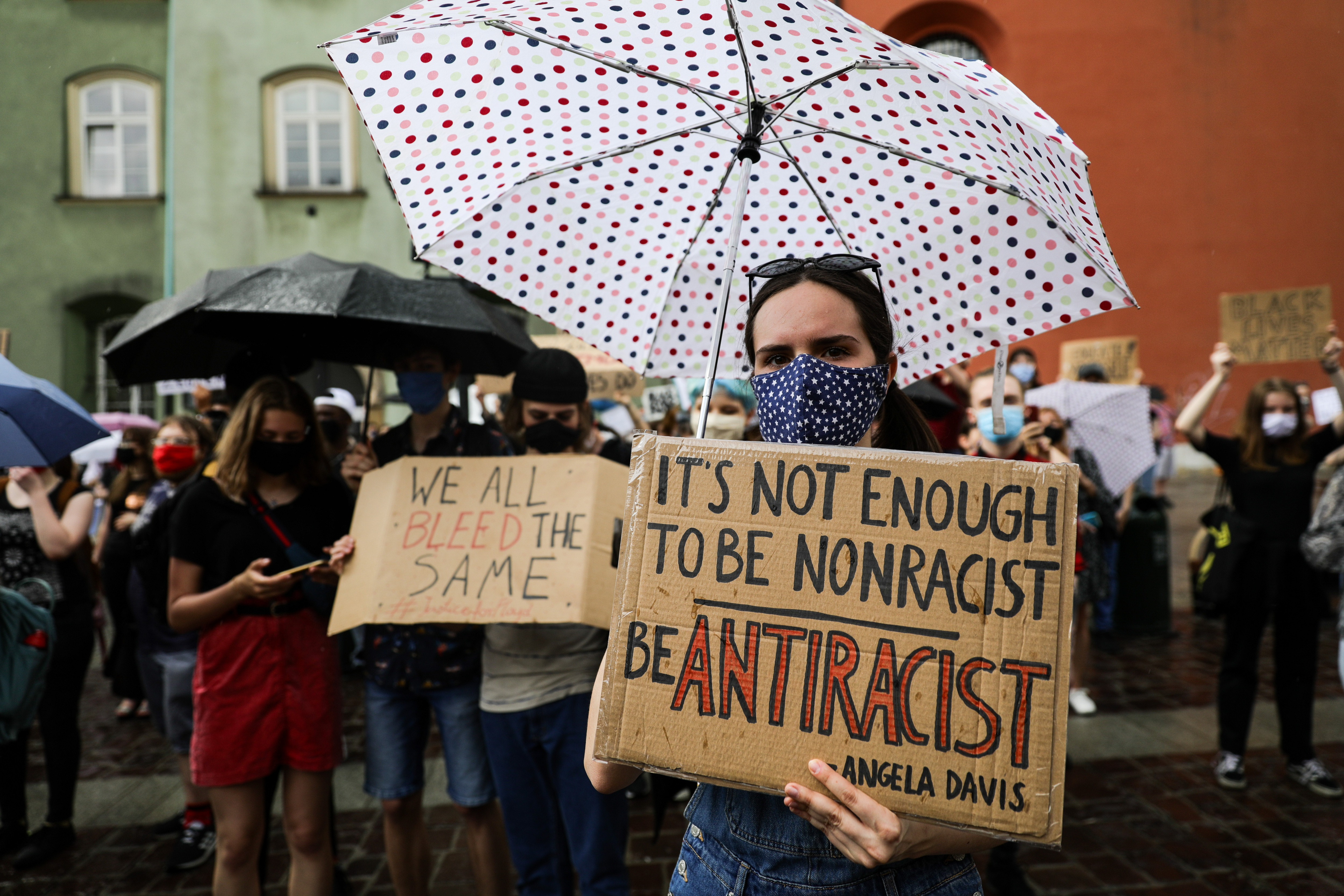 A protester wearing a facemask and holding an umbrella shows...