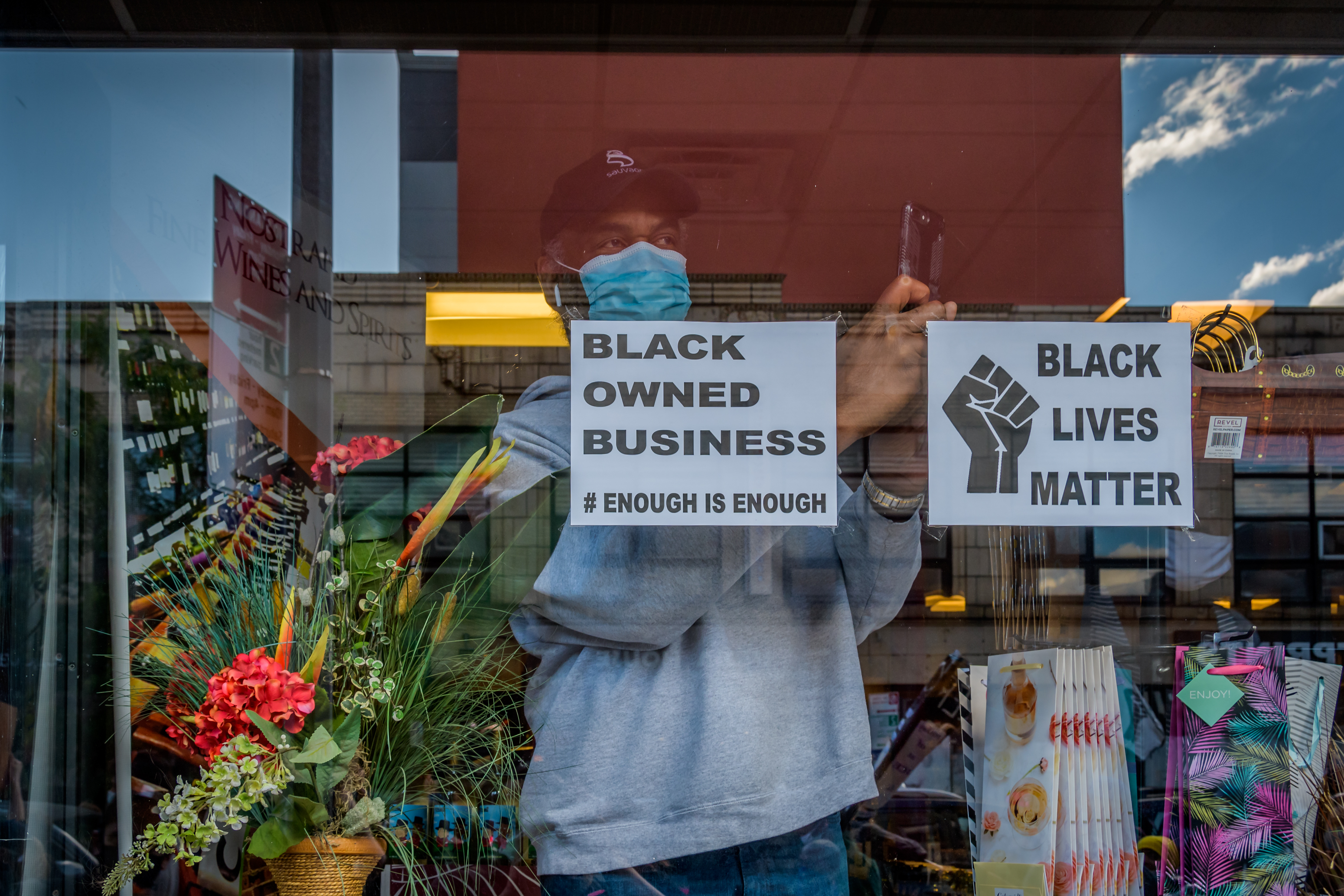 A&nbsp;man wearing a&nbsp;cap and&nbsp;mask&nbsp;stands inside&nbsp;of a&nbsp;black owned business&nbsp;in Crown Heights Brooklyn .
