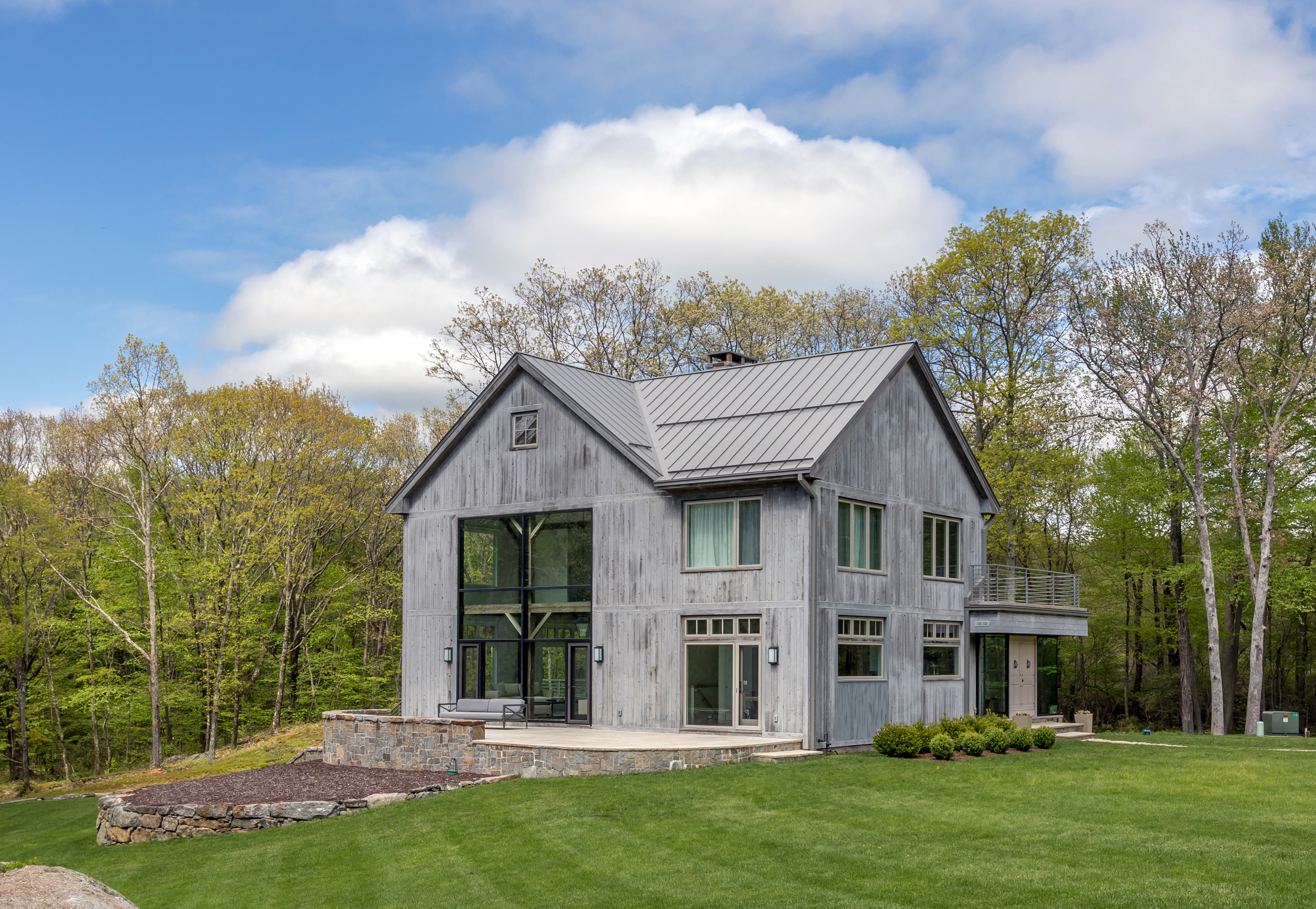 一个现代木材房子的外景有灰色壁板和大窗口的。有草和蓝天。