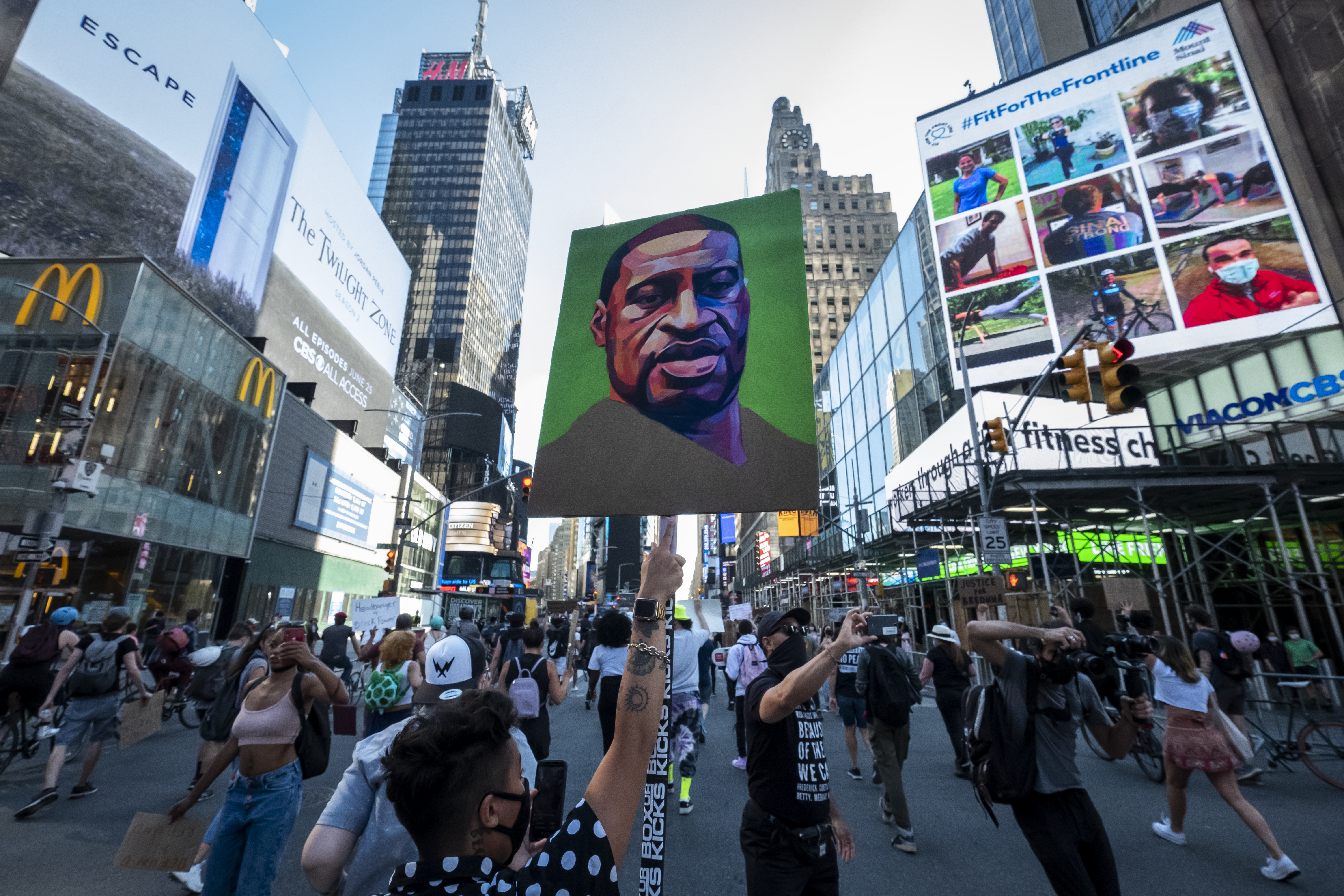 Protesters wearing masks walk through the streets of Times Square holding up their hands and chanting, “Hands Up Don’t Shoot” after police officers conceded to let protesters that are trying to peacefully march through Times Square with one protester holding a sign with a portrait painting of George Floyd.