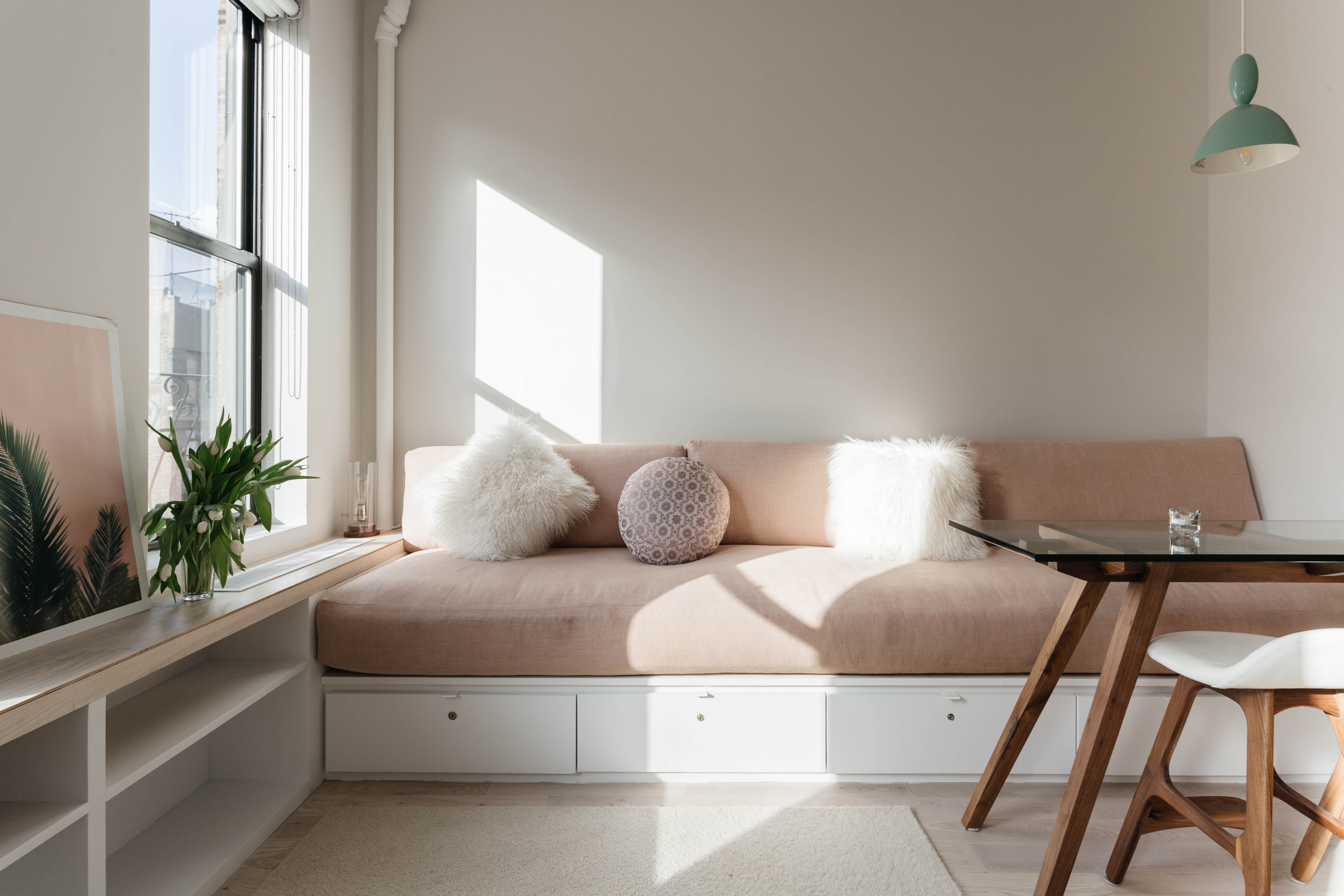 A dusty pink couch in a living room with a window and a glass coffee table.