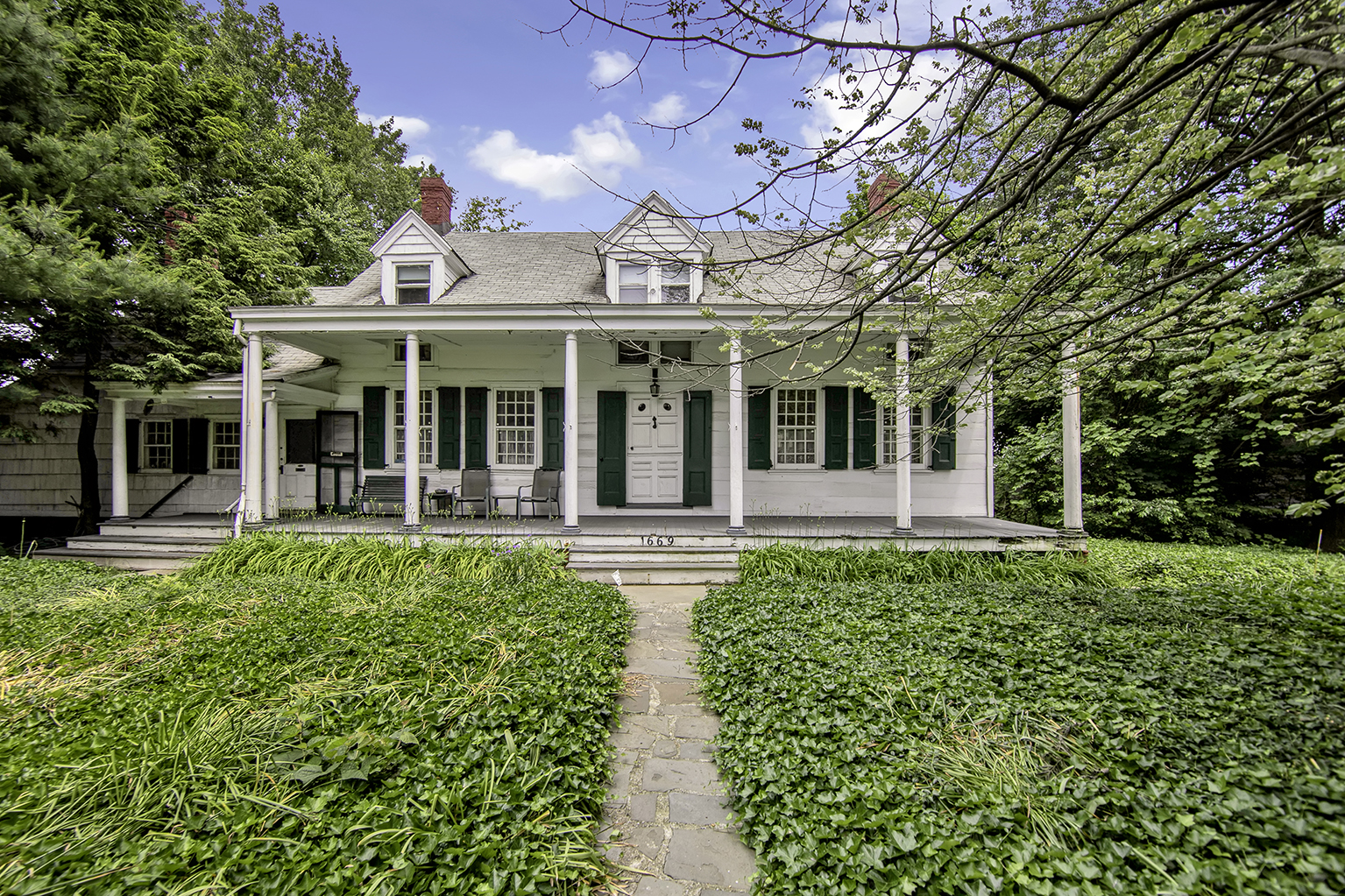 A farmhouse with a large front garden, and a porch with columns.