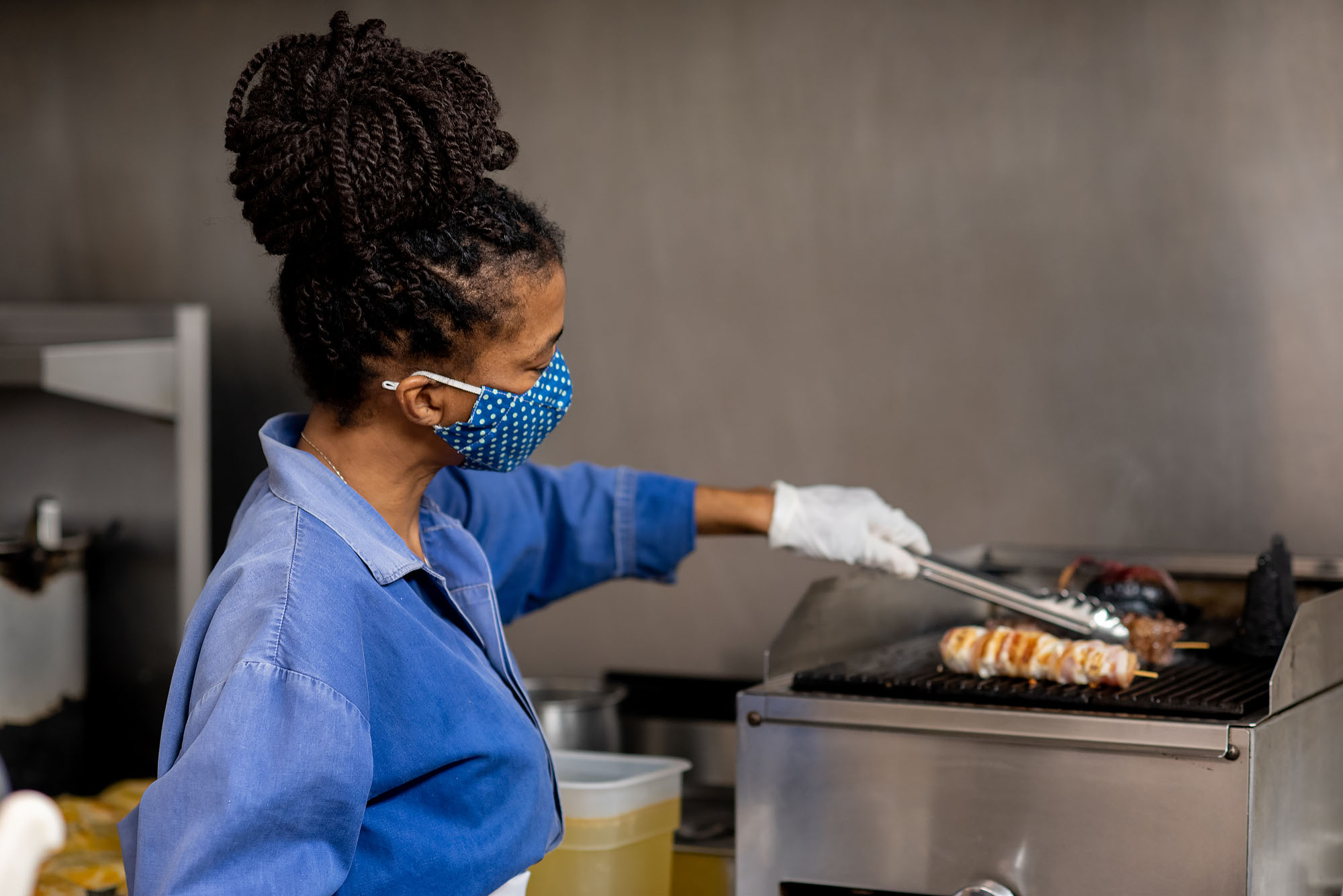 Natalia Pereira, chef and owner of Wood Spoon restaurant in Downtown LA, wearing a cloth mask and grilling meats in the kitchen.