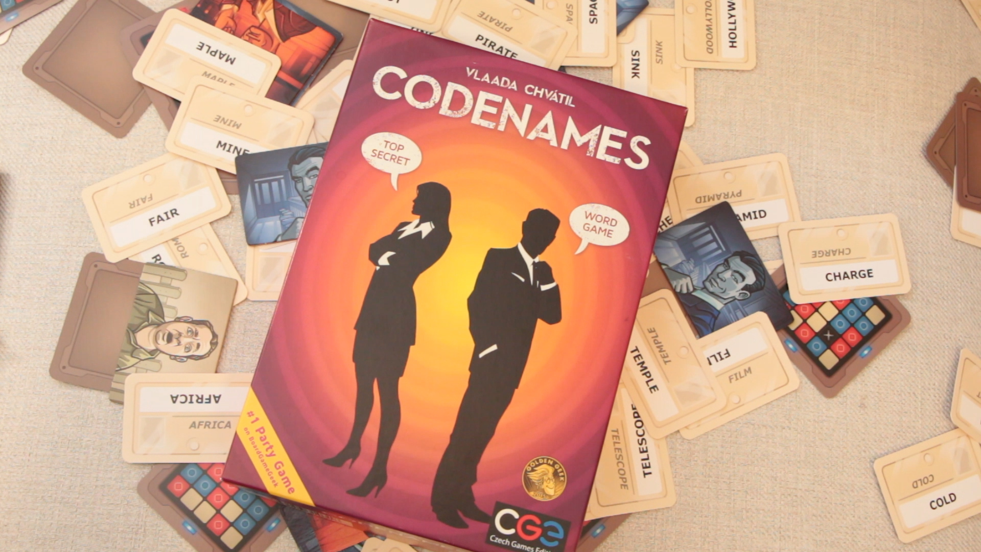 A box for the board game Codenames lays on a messy pile of cards from the game.