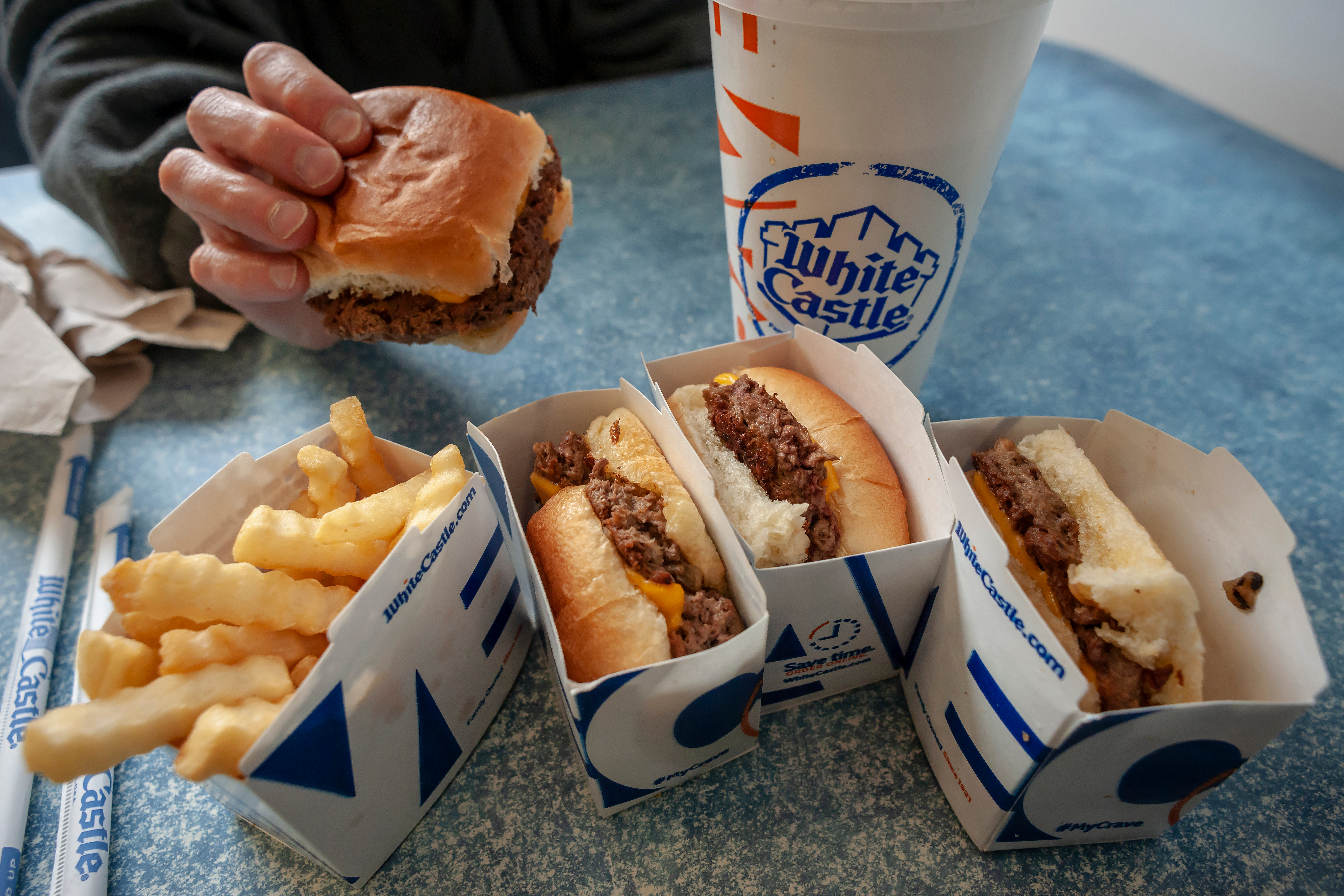Hand holding White Castle slider, on a table with other White Castle food.