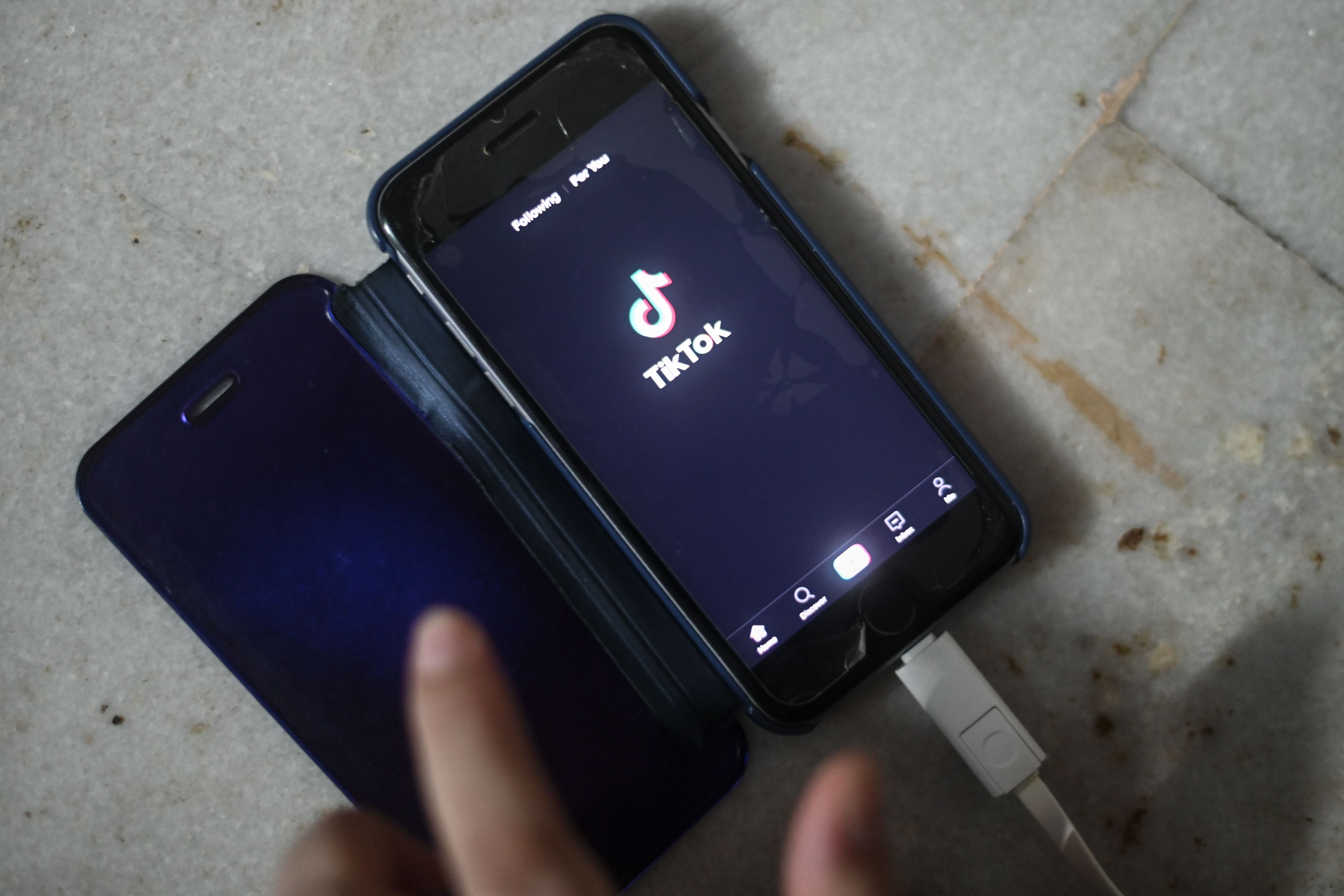 A finger hovers over the screen of a phone displaying the TikTok app.