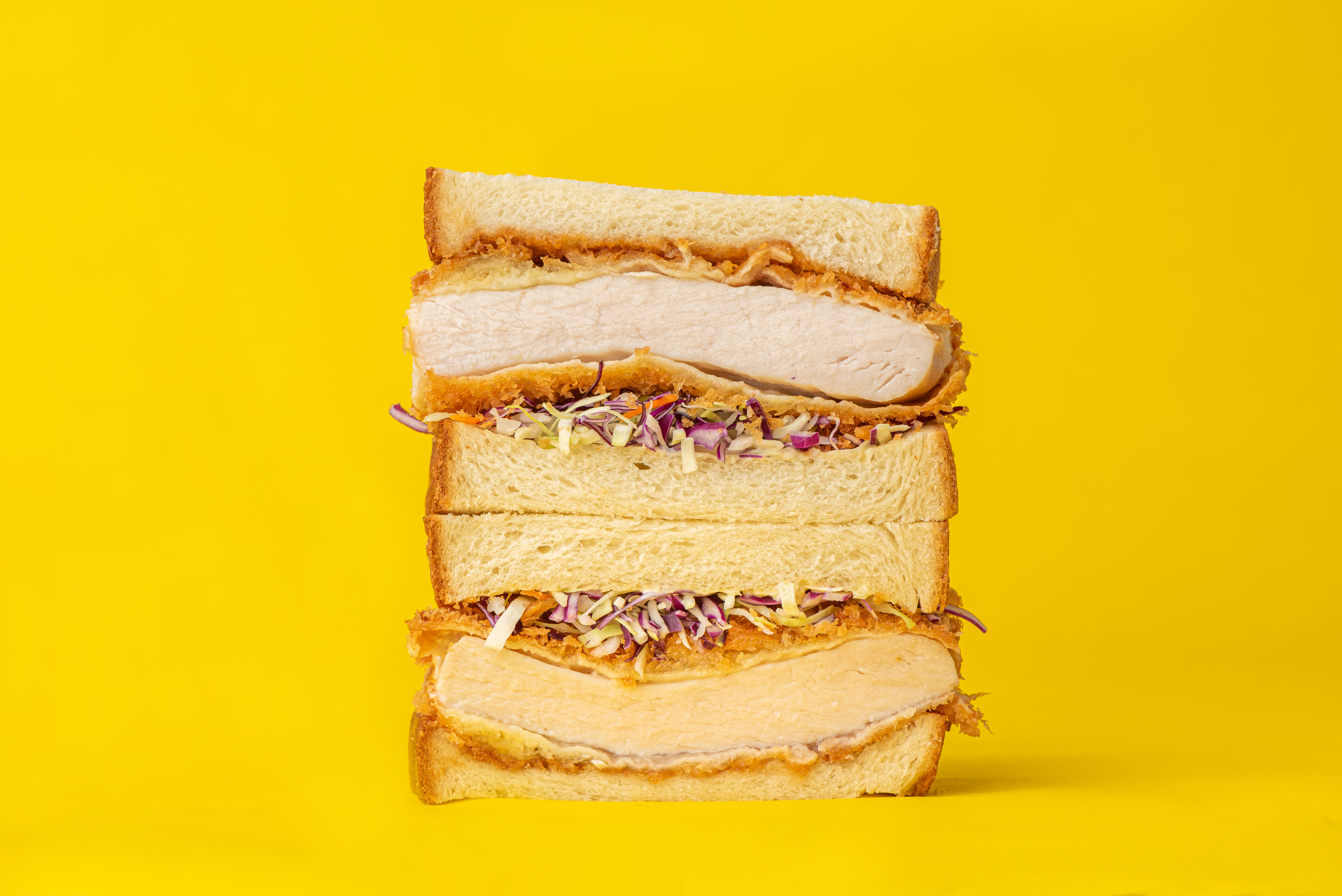 A pork katsu sandwich stacked high with a yellow background.