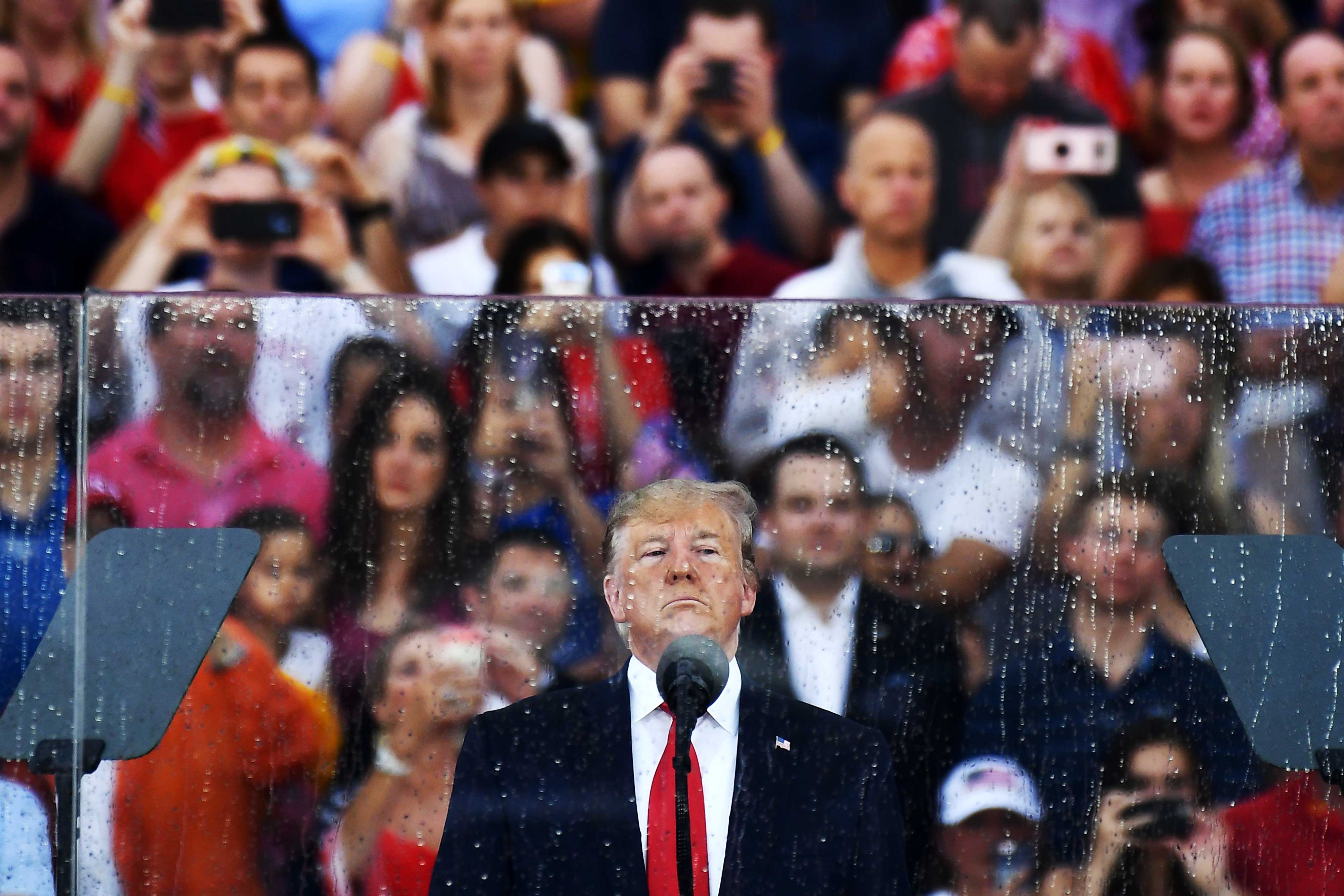 Trump, in a navy suit and bright red tie, scowls in front of a microphone. Behind him is bulletproof glass, wet from rain. And behind the glass, a crowd of cheering Trump supporters wearing red, white, and blue.