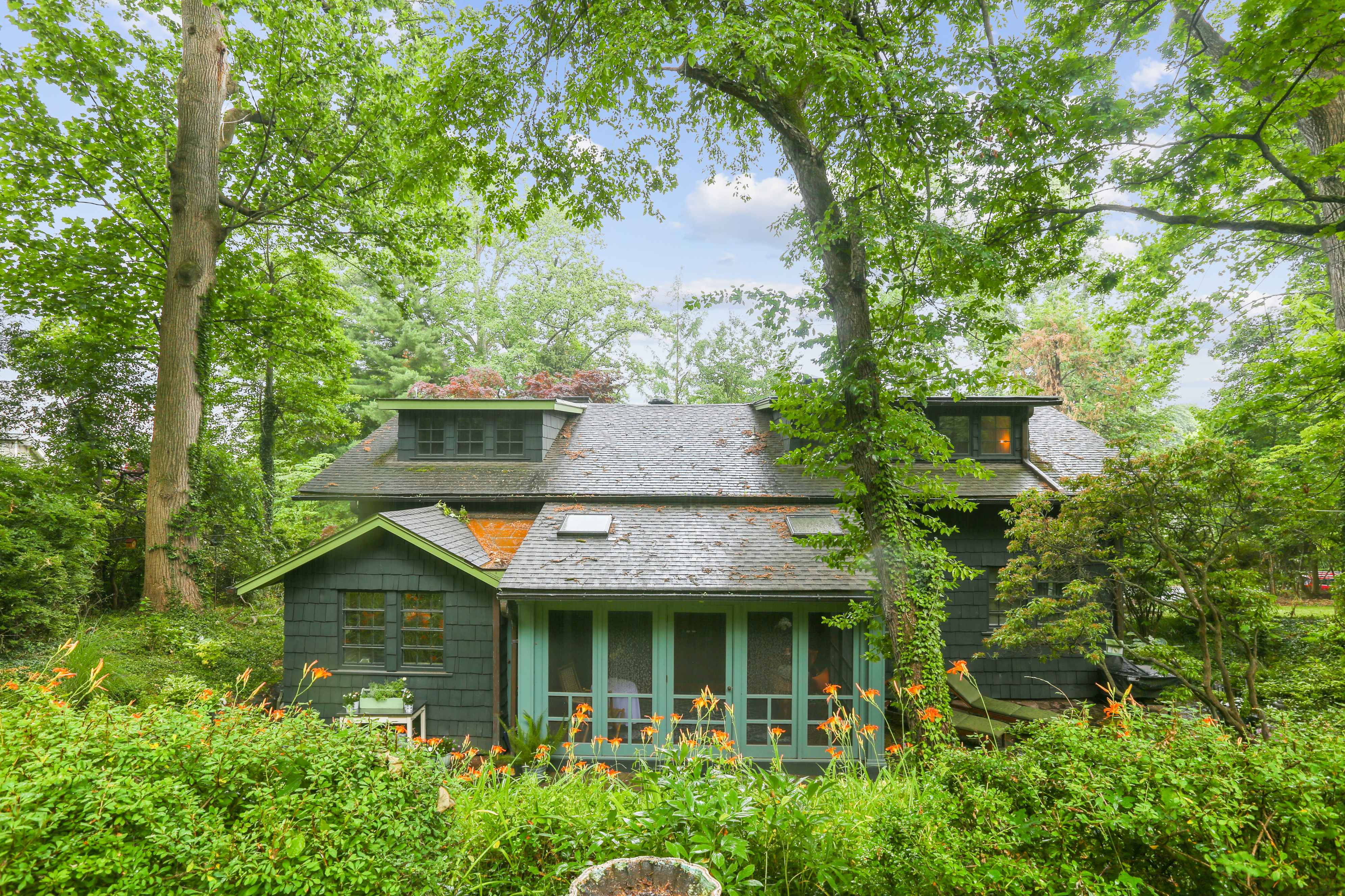 An exterior view of an Arts and Crafts style home that sits surrounded by green foliage. 