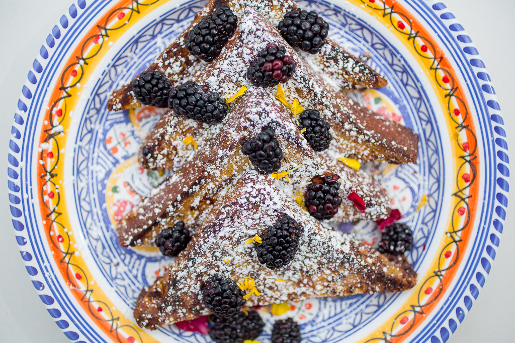A blue plate with orange and red trim filled with French toast topped with blackberries and powdered sugar
