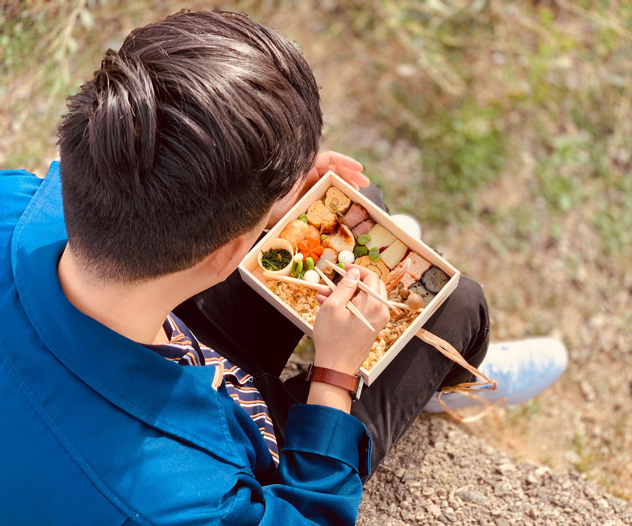 Man sitting outdoors with a bento box in his lap.
